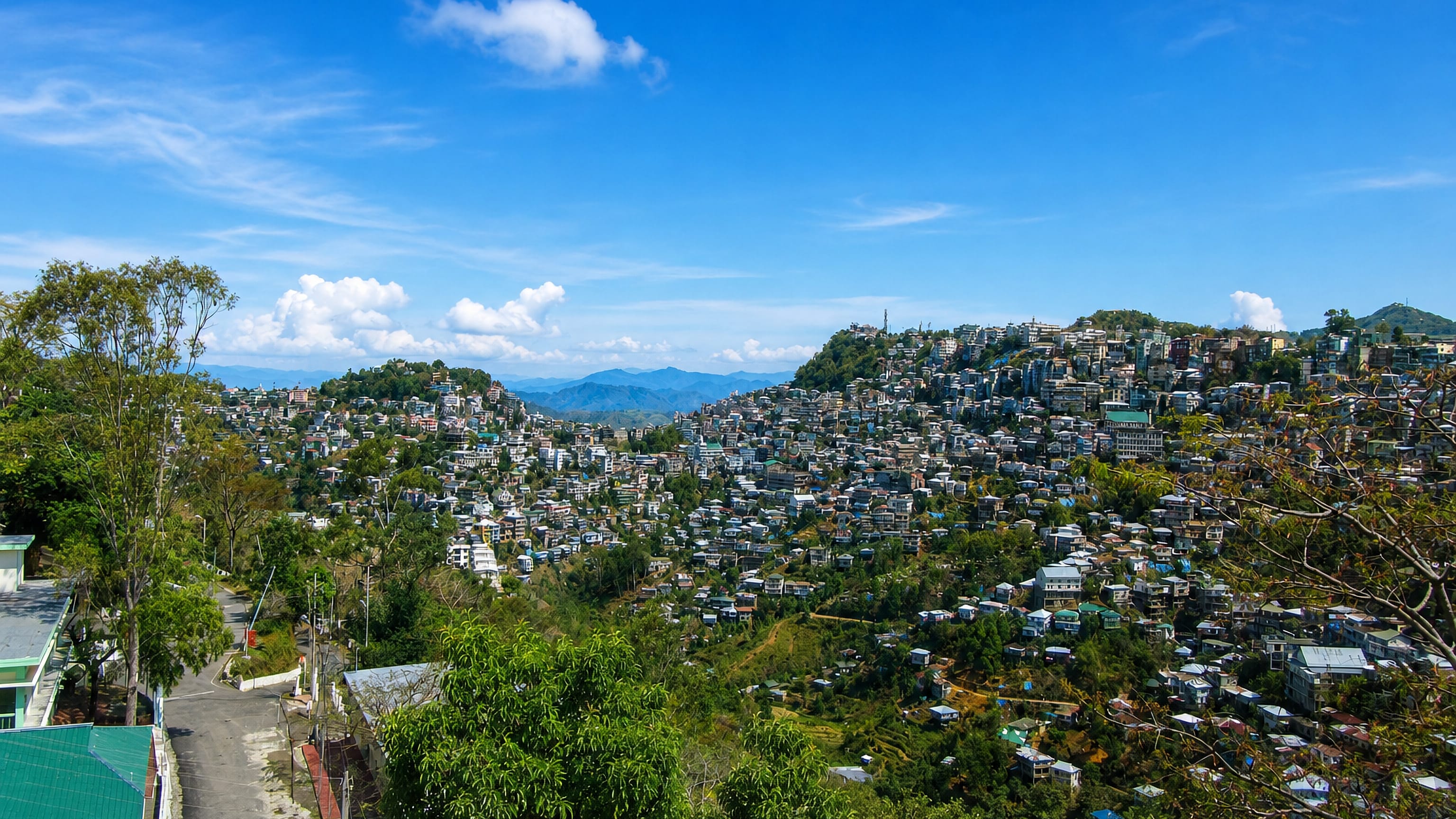 Hillside homes of Aizawl stacked along forested ridges in Mizoram under a bright blue sky