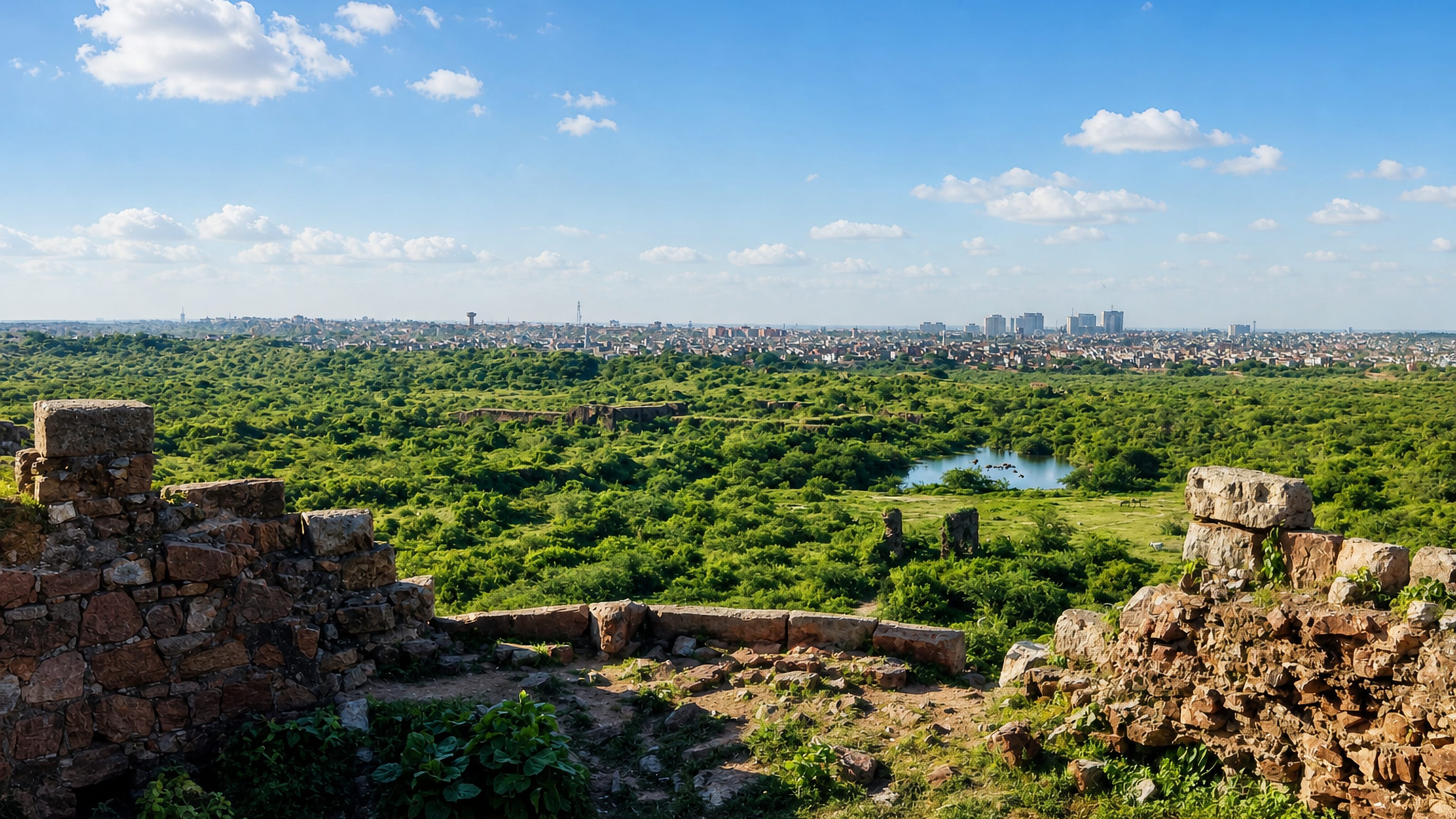 Ruined stone ramparts above green scrubland on the Delhi ridge near Okhla, with the city skyline beyond.