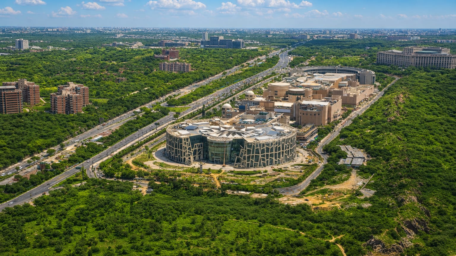 Aerial of Vasant Kunj, New Delhi, showing a circular glass building set among wooded ridge greenery and highways