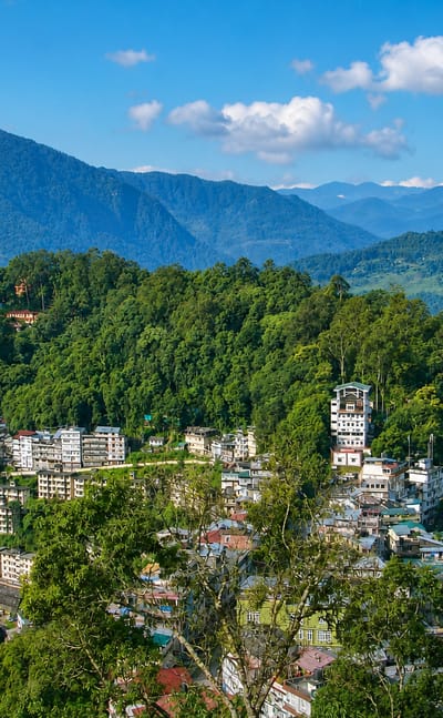 Gangtok's hillside houses on a forested ridge with a ropeway cable and Himalayan peaks beyond in Sikkim.