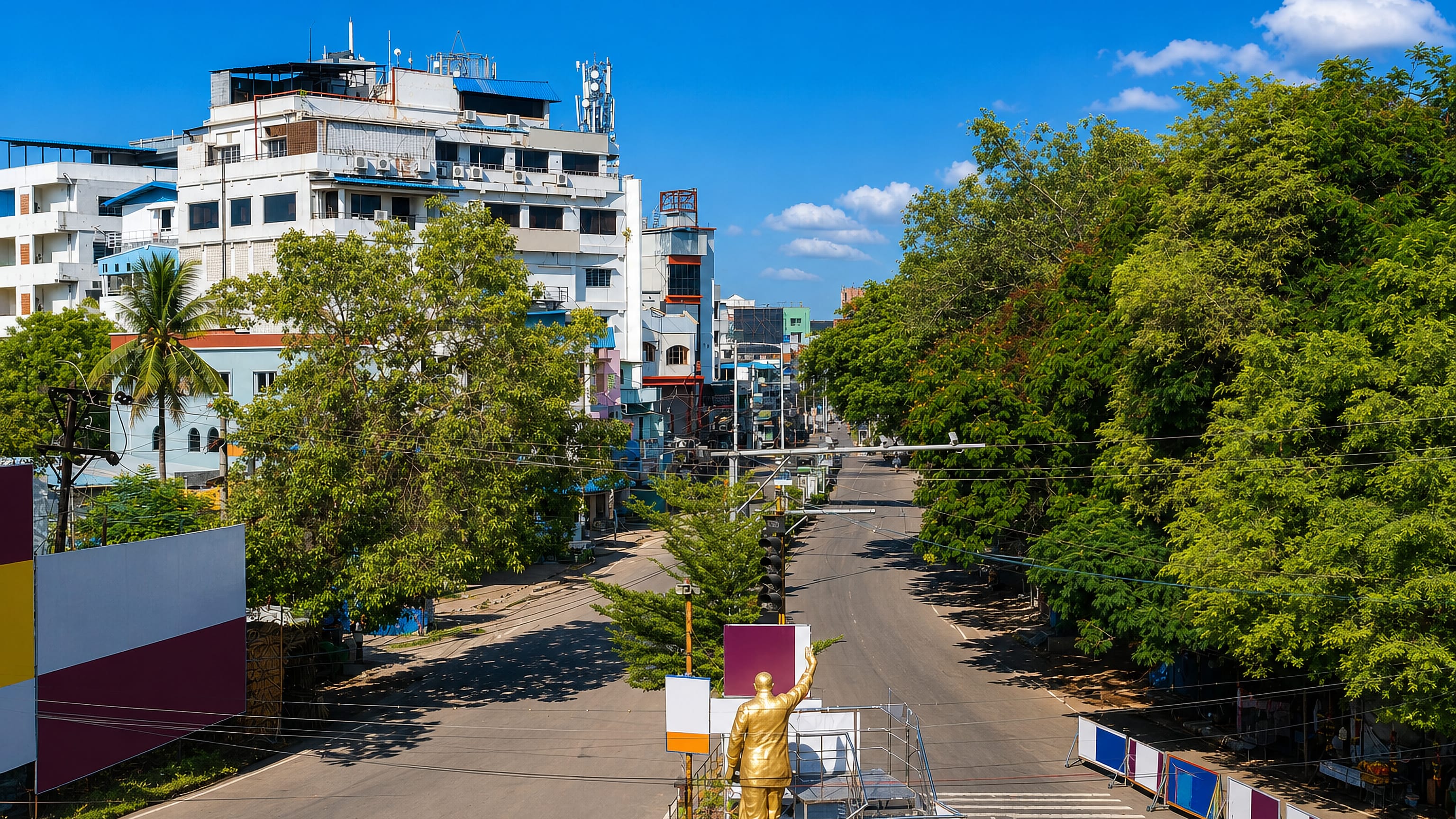 Golden statue on a traffic island at a wide tree-lined junction in central Eluru, India.