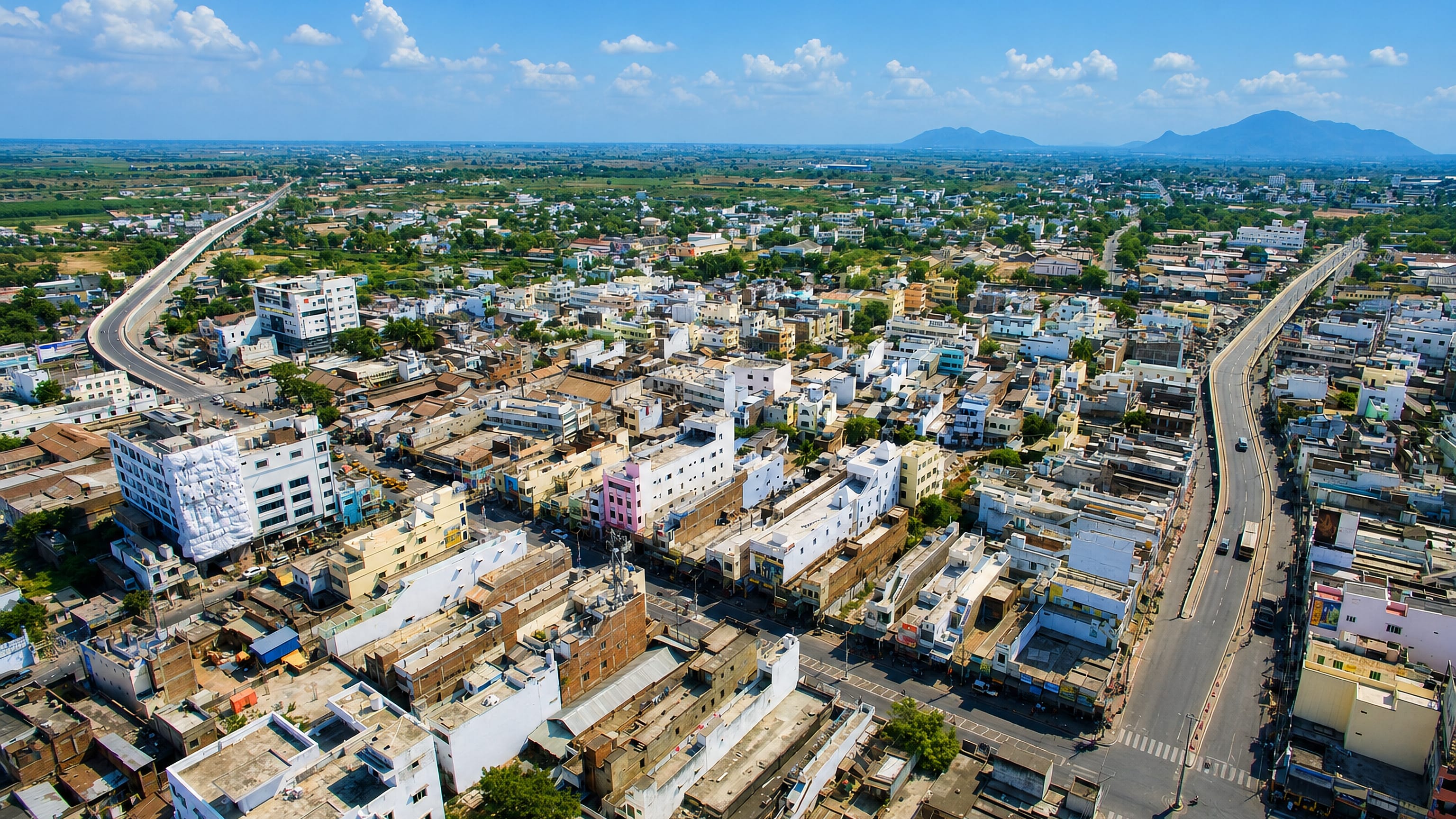 Aerial view over Narasaraopet's dense rooftops and elevated highway with Andhra Pradesh hills beyond.