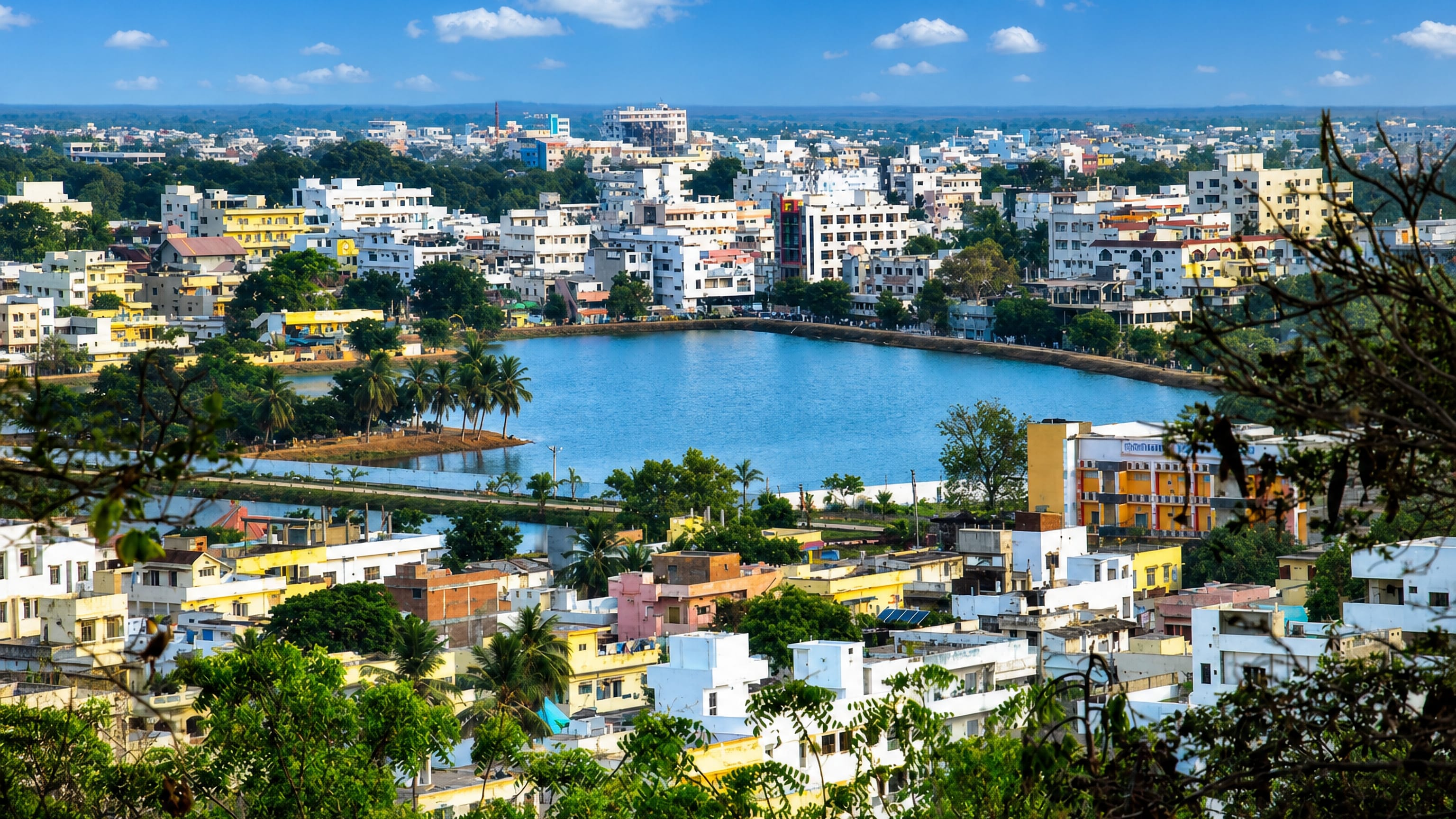 Hilltop view over Ongole, its central tank ringed by pastel houses and palms under a clear sky.