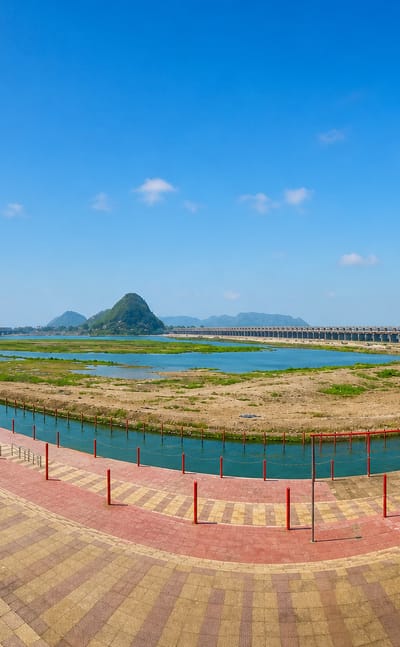 Riverfront promenade in Vijayawada, India, overlooking the Krishna River with a barrage and a green hill beyond.
