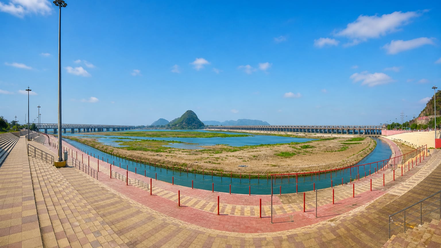 Riverfront promenade in Vijayawada, India, overlooking the Krishna River with a barrage and a green hill beyond.