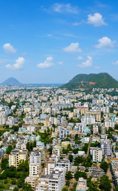 Aerial view of Visakhapatnam, India, a dense mid-rise city among green hills beside the sea
