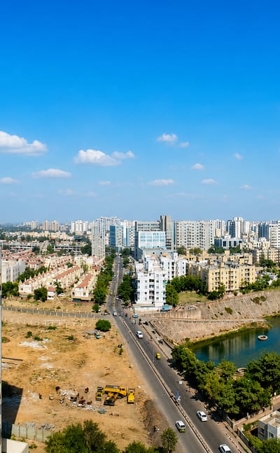 Aerial daytime view of Ahmedabad's residential towers, low-rise housing and green suburbs under scattered clouds.