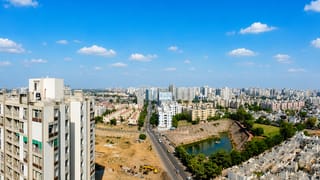 Aerial daytime view of Ahmedabad's residential towers, low-rise housing and green suburbs under scattered clouds.