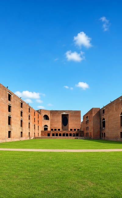 The brick arcades of the IIM Ahmedabad campus in Ahmedabad's West Zone, seen across a green lawn