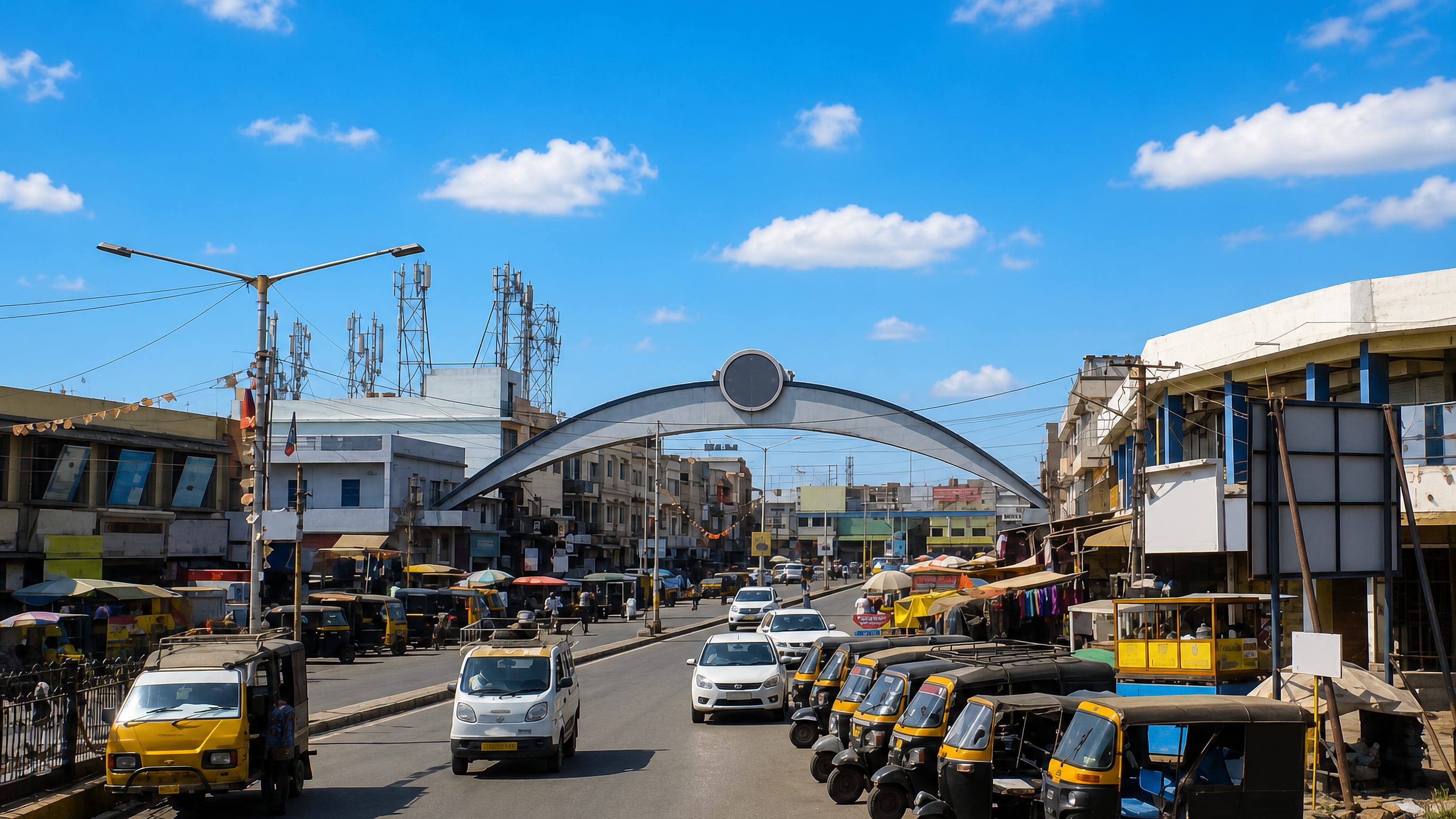 Traffic and auto-rickshaws passing under a steel gateway arch on a market street in Gāndhīdhām, Gujarat.
