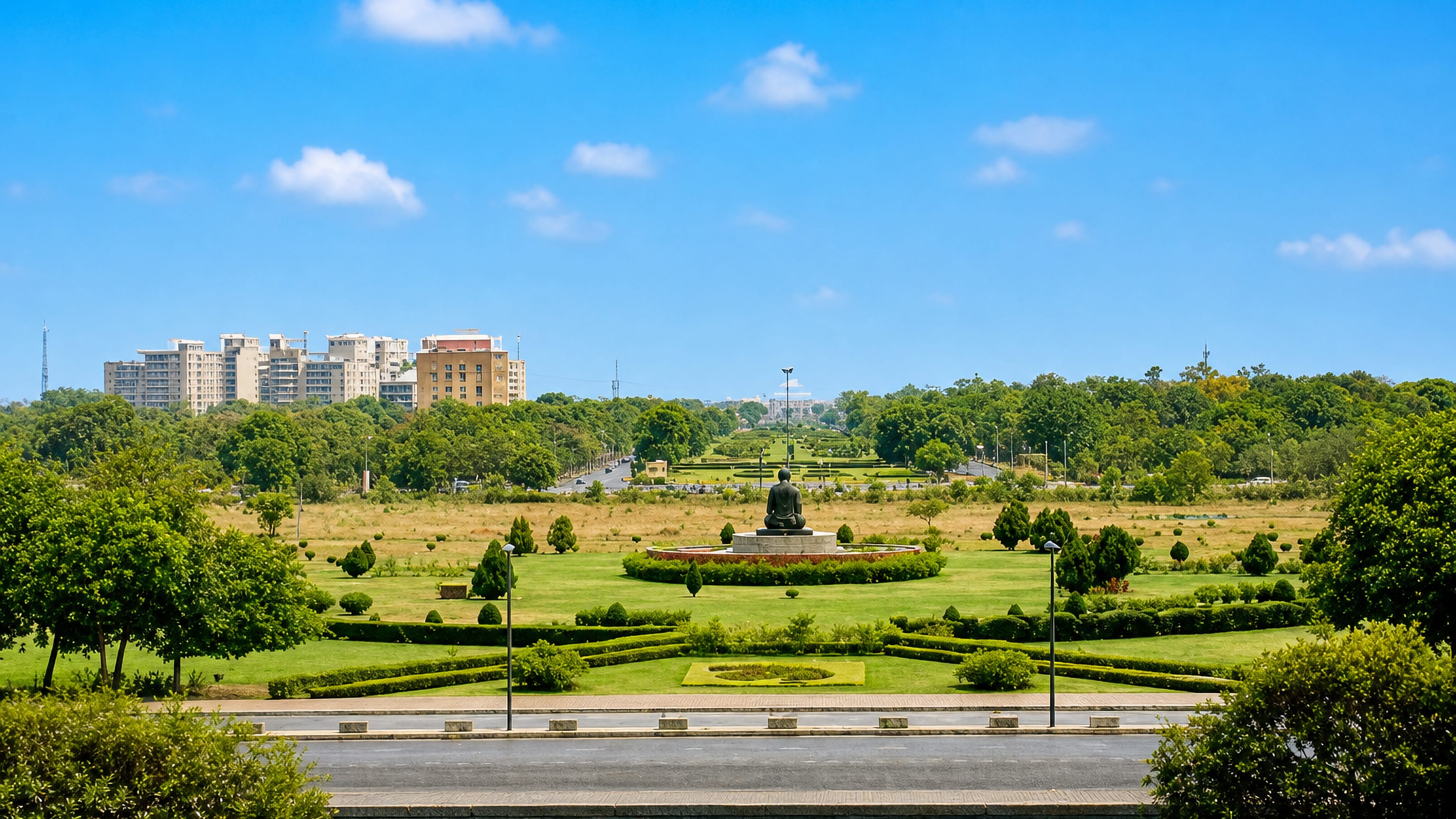 Landscaped gardens and a seated bronze statue in Gandhinagar, India, with apartment blocks beyond the treeline