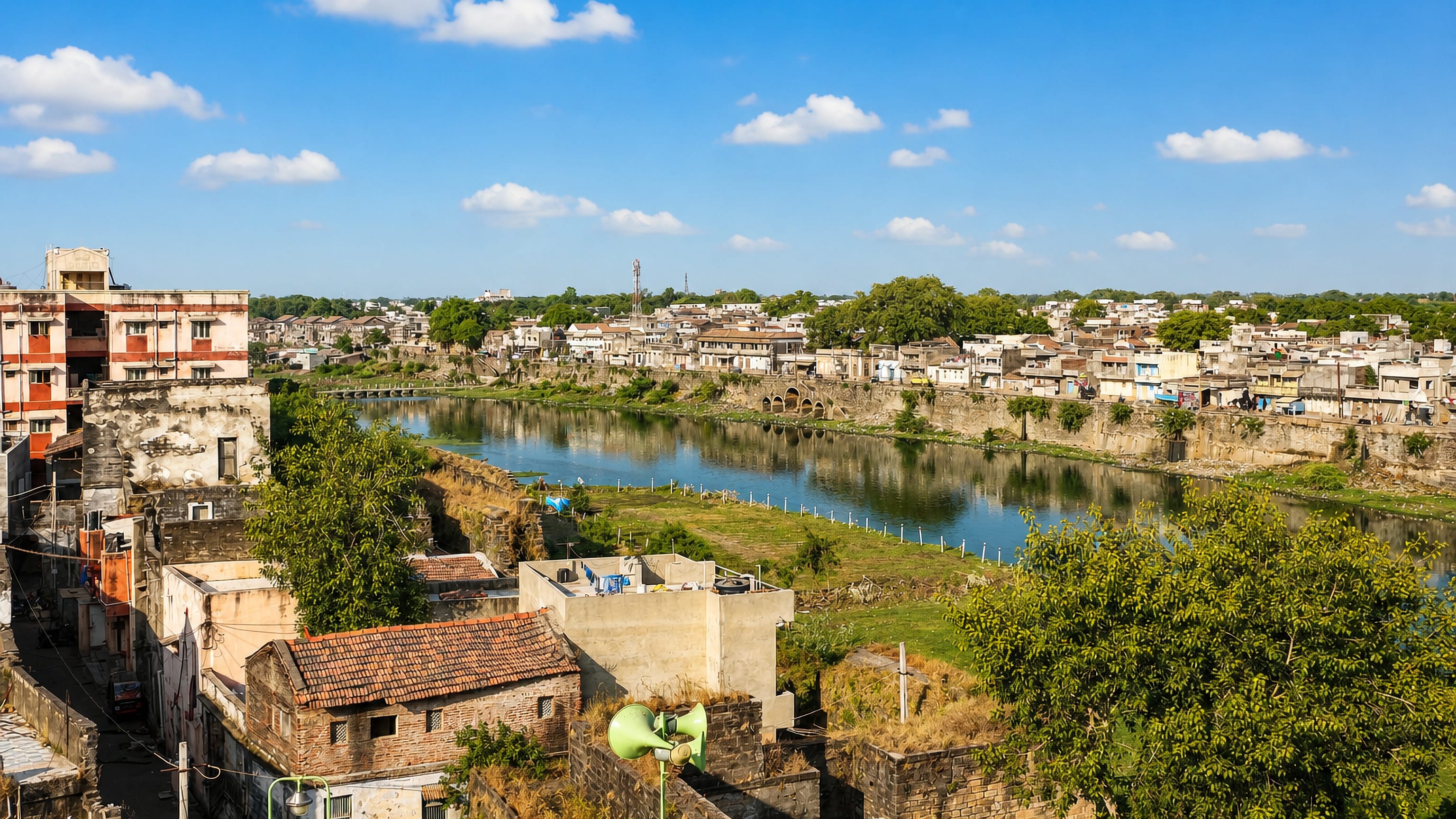 Rooftop view across Gondal, Gujarat, over stone embankments and the town's river to low houses and trees.