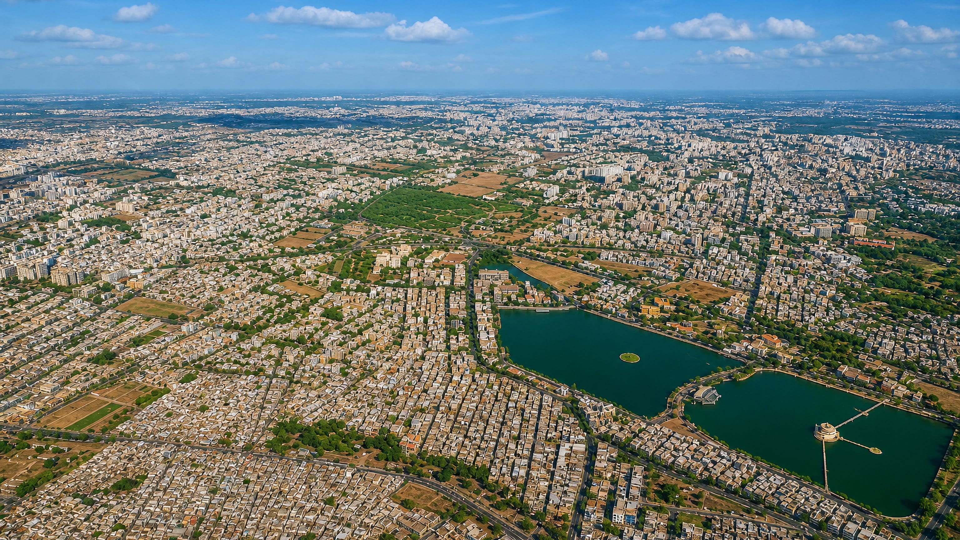 Aerial view of Jamnagar spread around Ranmal Lake and its island fort under a clear blue sky.