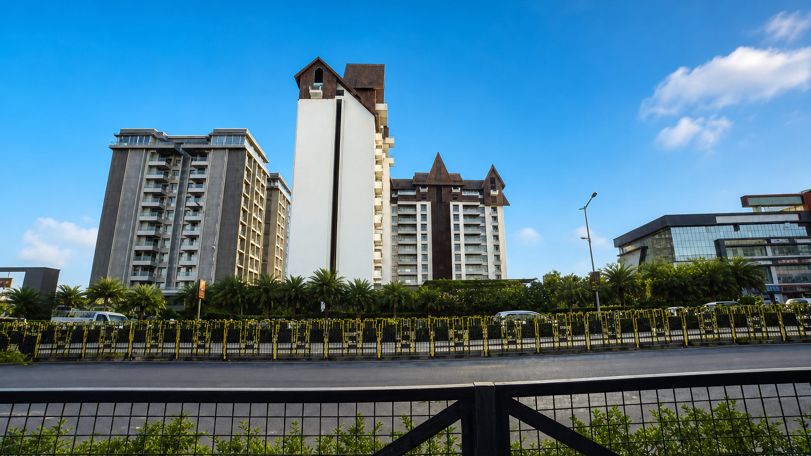 High-rise apartment towers and a palm-lined boulevard in a modern residential quarter of Rajkot, Gujarat.