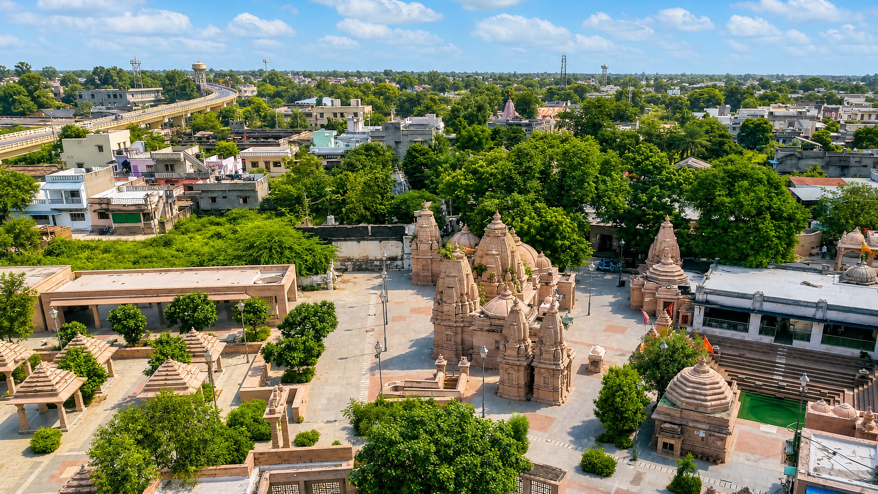 Sandstone temple spires and pavilions above the rooftops of Siddhapur, Gujarat, with a flyover beyond.