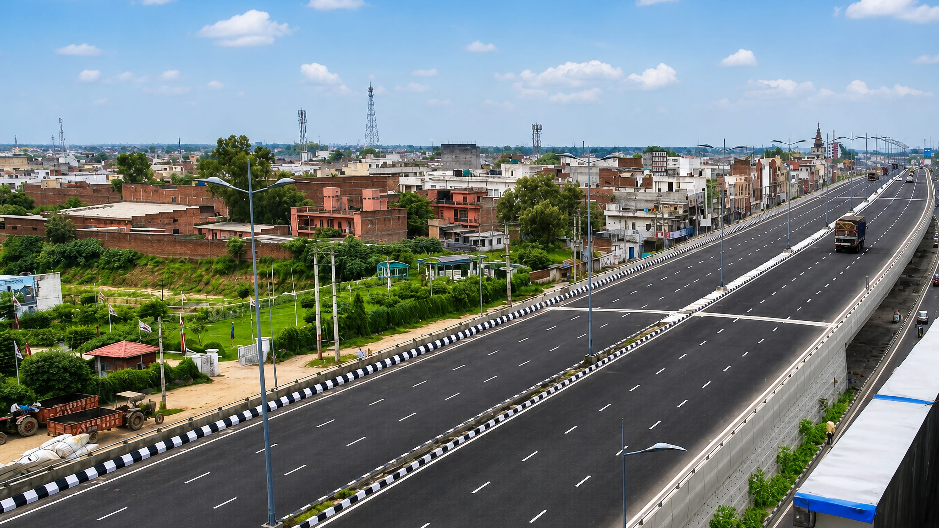 A broad divided highway running past the brick rooftops and distant temple spire of Panipat, Haryana.