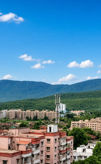 Jamshedpur's apartment blocks and greenery spread below forested Dalma hills under a blue sky.