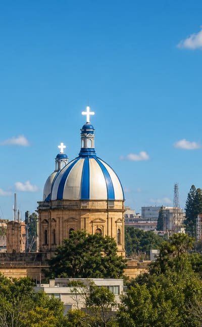 Blue-and-white church domes topped with crosses rising above tree-lined Bengaluru cityscape.