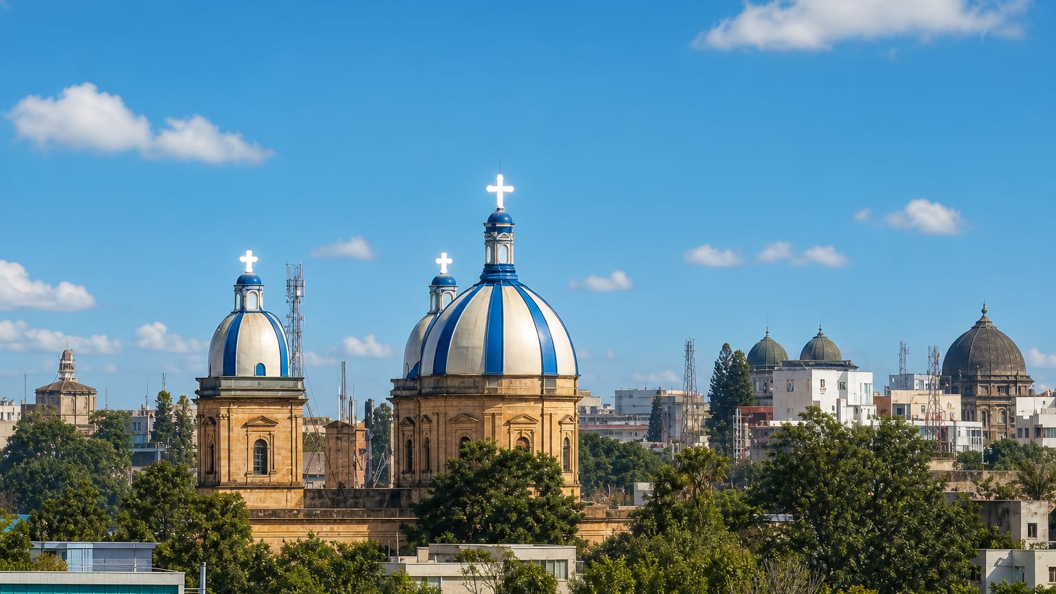 Blue-and-white church domes topped with crosses rising above tree-lined Bengaluru cityscape.