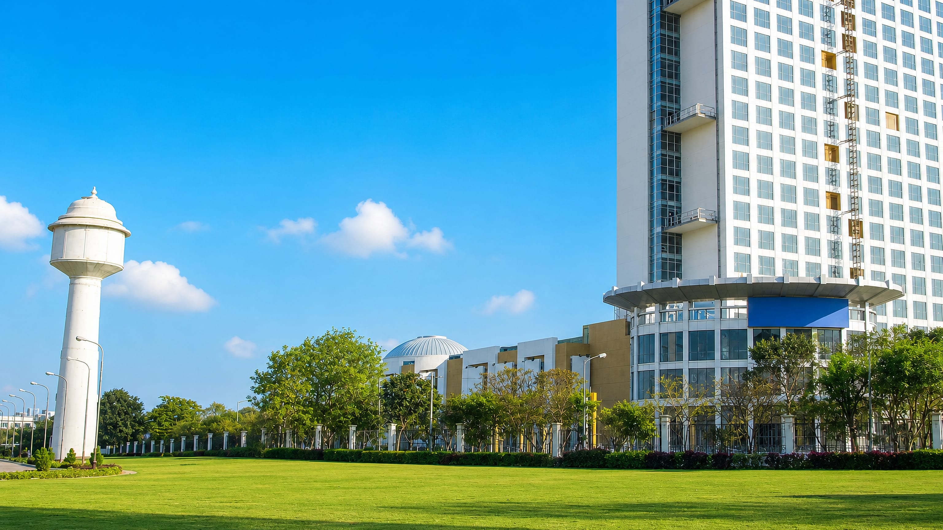 A high-rise tower and water tower above open lawn in Whitefield, Bengaluru, India.