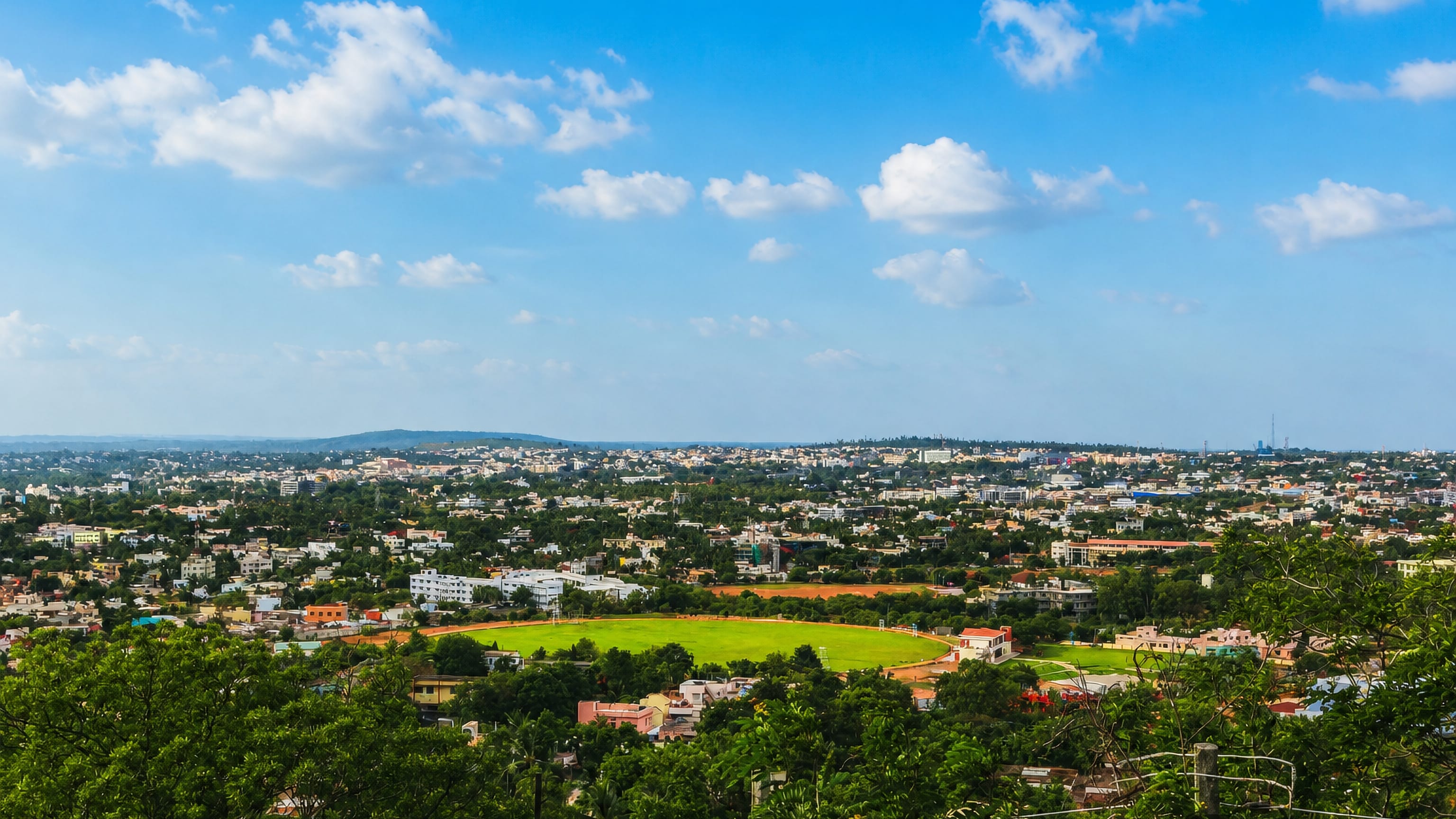 Hilltop view over Hubballi, Karnataka, with a green sports ground ringed by low-rise houses and trees.