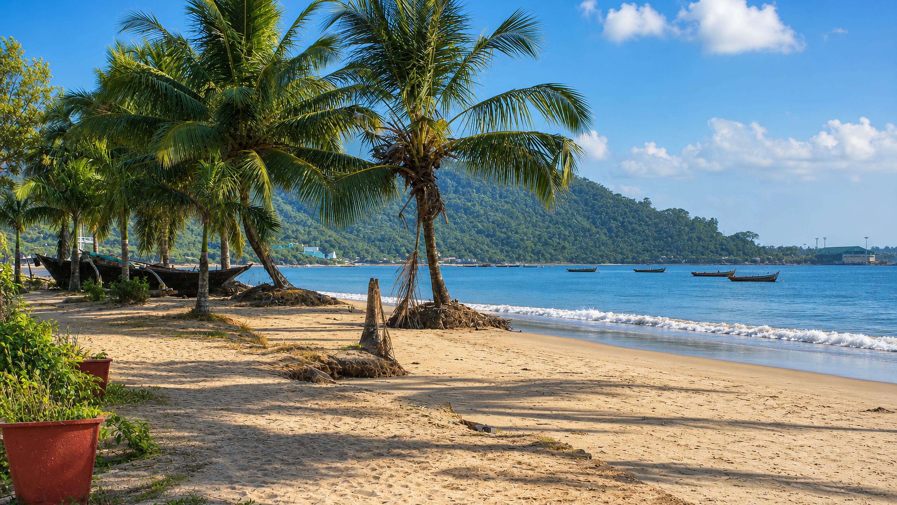 Palm-fringed sandy beach at Karwar on the Karnataka coast, with wooden fishing boats and a forested headland beyond.
