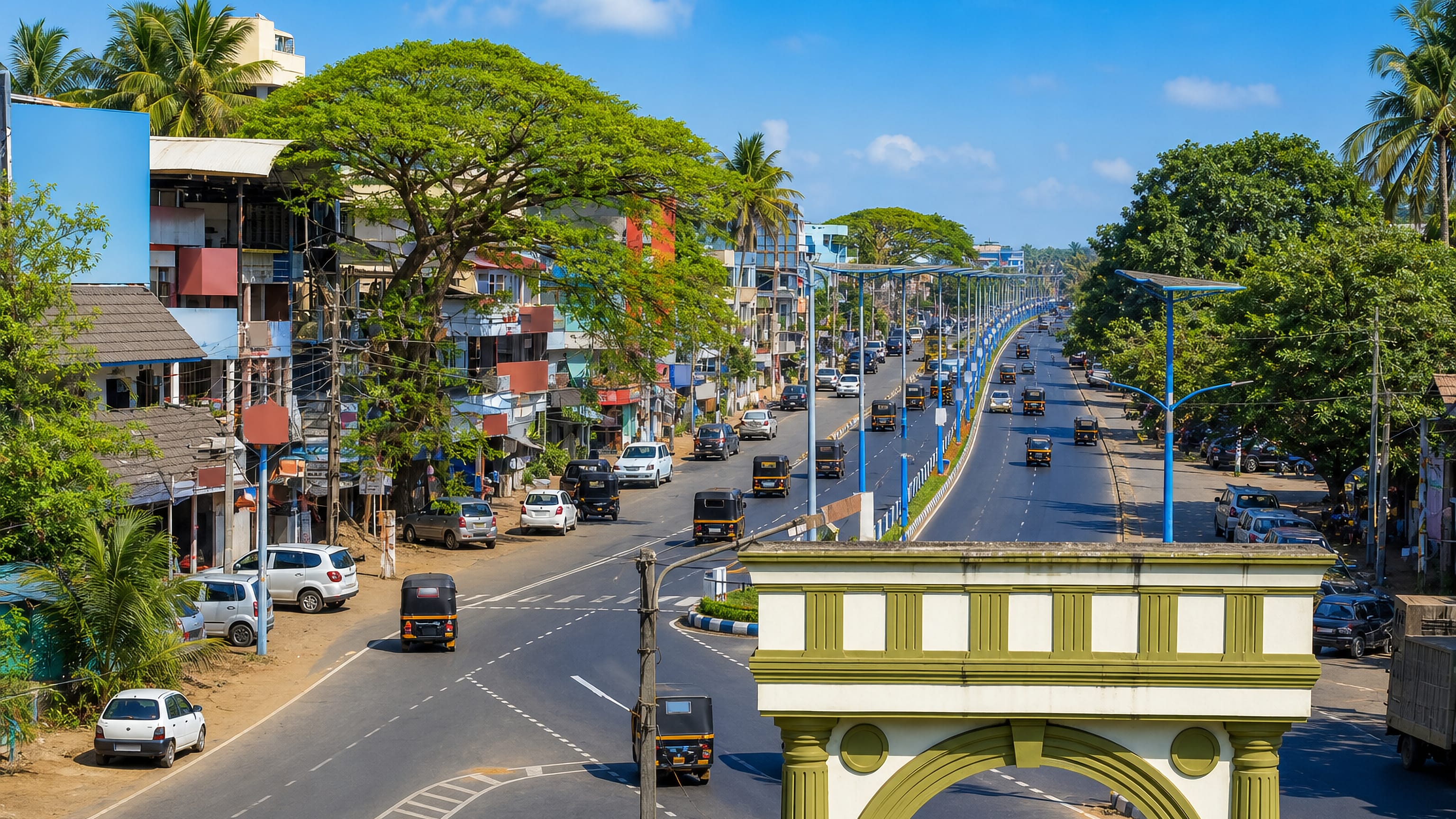 Divided highway through Kāsaragod, Kerala, lined with palms, shopfronts and autorickshaws.