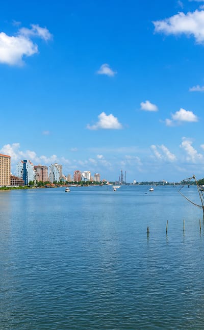 Kochi waterfront with high-rise towers and traditional Chinese fishing nets over the Kerala backwaters.