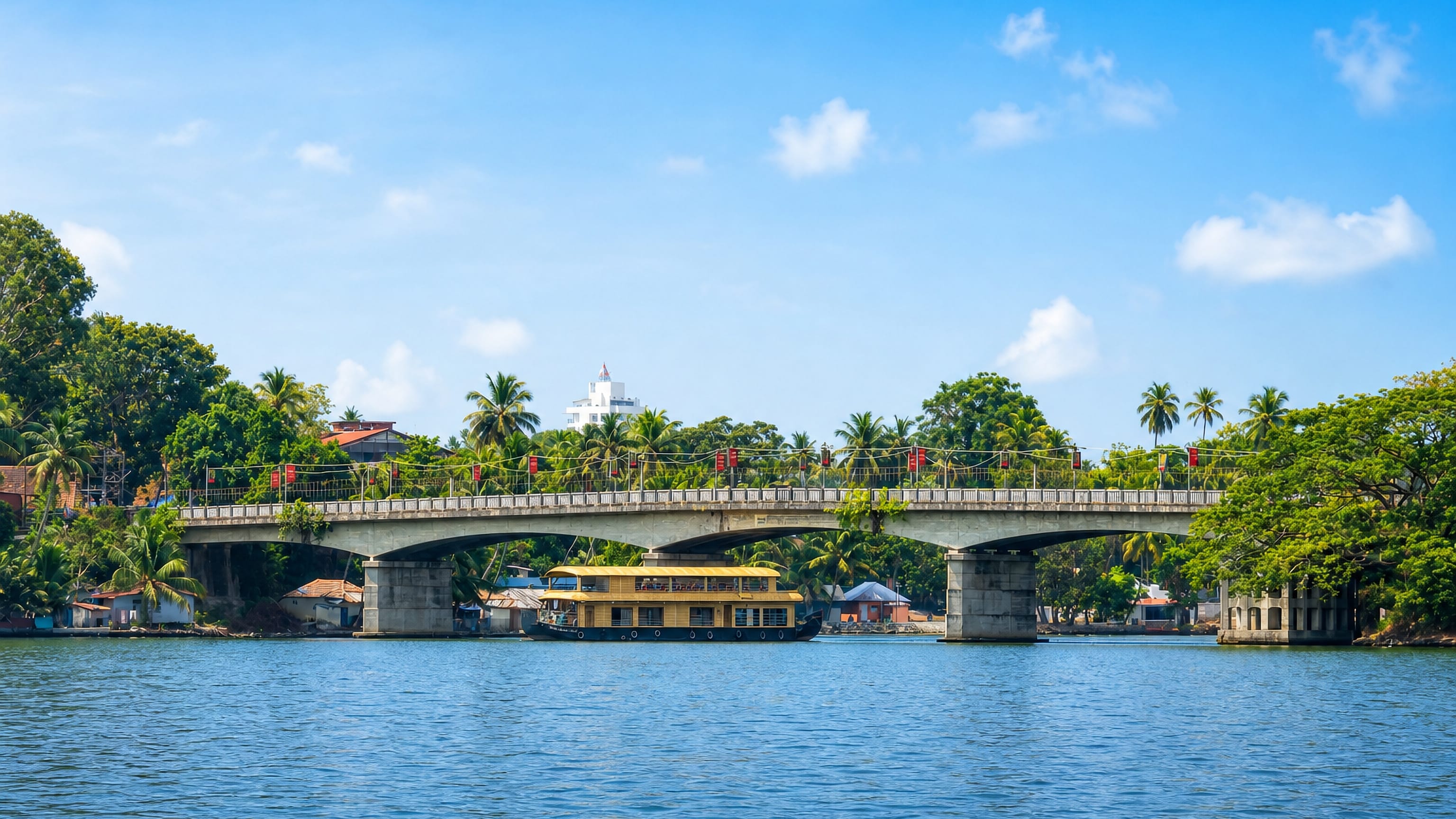 Concrete road bridge over the backwaters at Kollam, Kerala, with a houseboat moored beneath the palms.