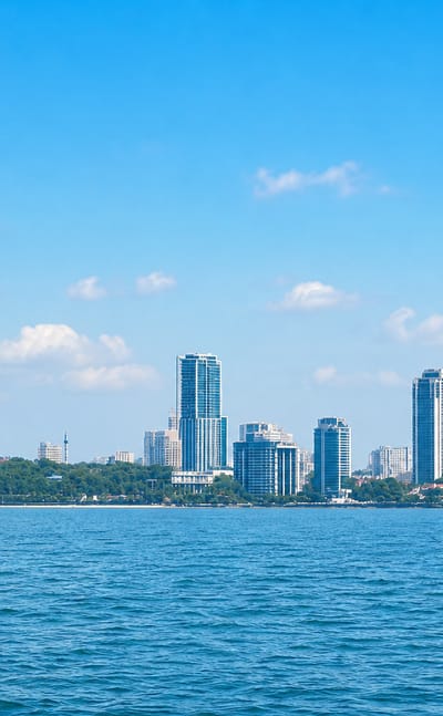 Cluster of glass high-rise towers along a waterfront at Kozhikode, seen across calm blue water.