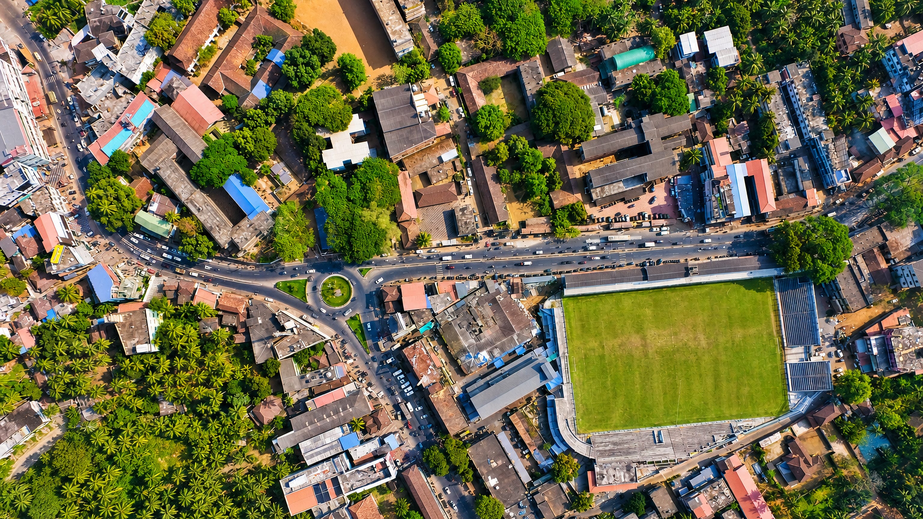 Overhead view of Malappuram, Kerala, showing dense tiled rooftops, palm groves, a roundabout and a football ground.