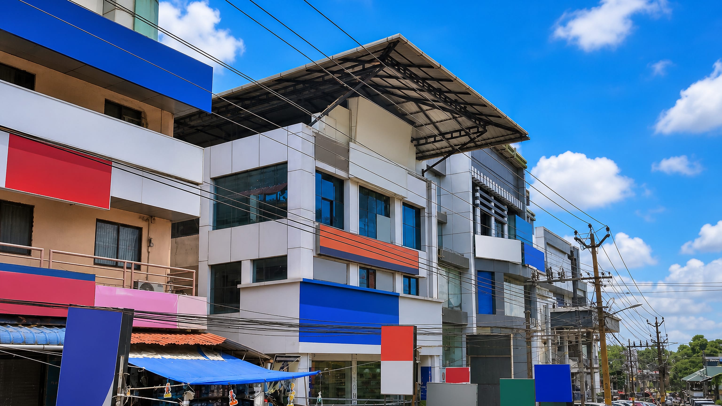 Concrete shophouses and market stalls along a busy street in Ottapalam, Kerala, under a bright blue sky.