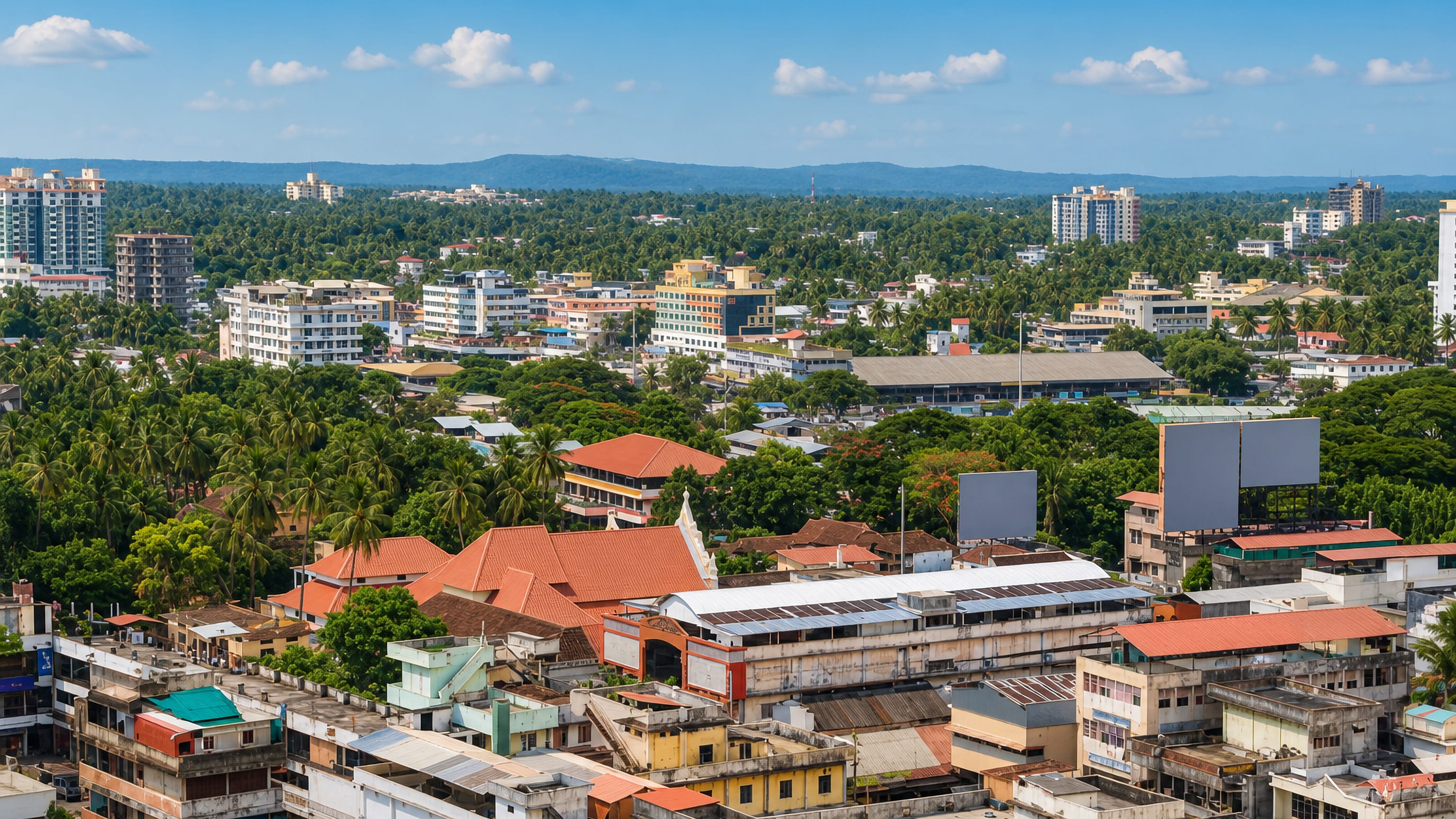 Thrissur's low-rise rooftops and coconut palms spreading toward distant hills in Kerala, India.