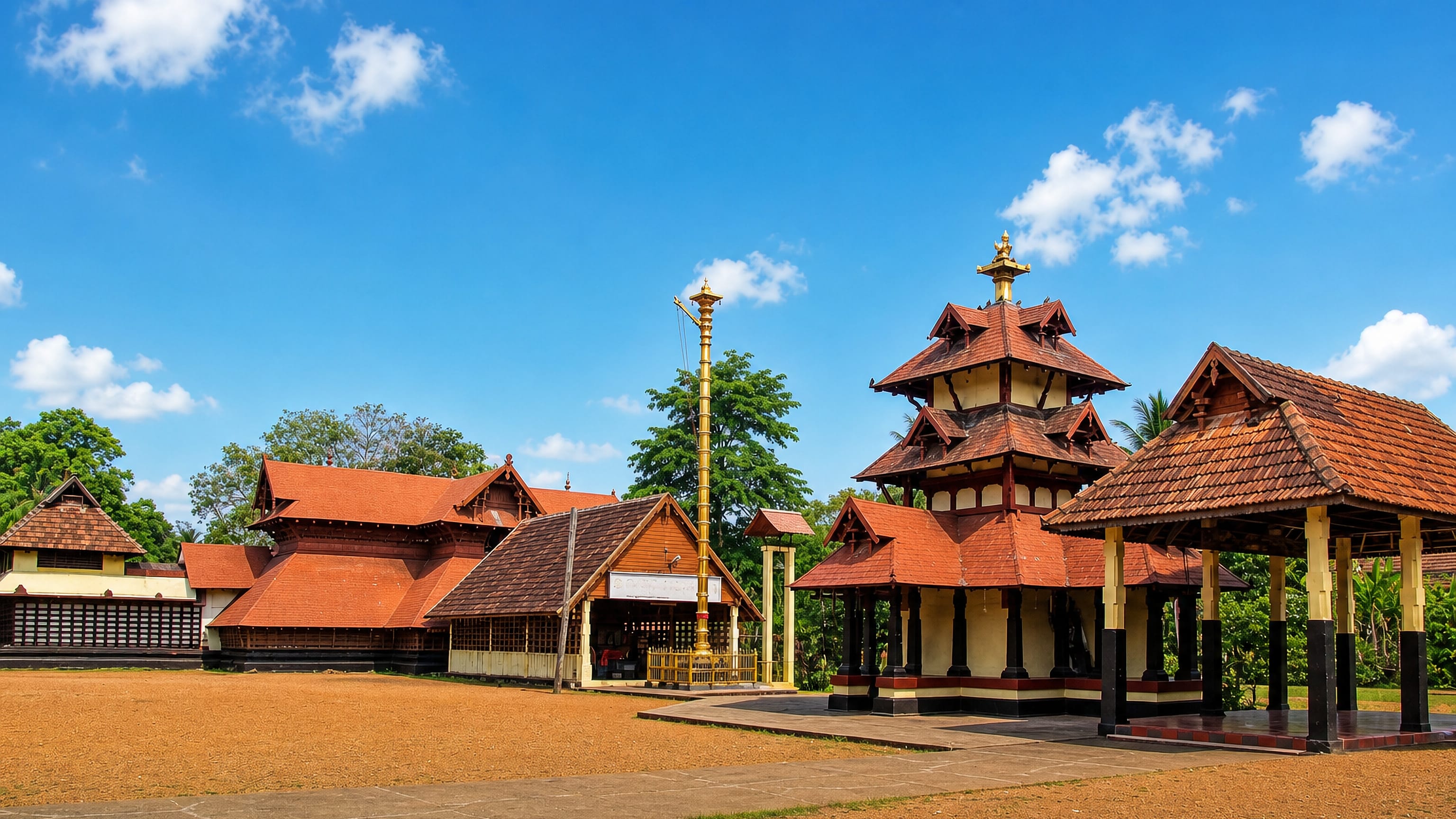 Tiled Kerala temple roofs and a golden flagstaff at a traditional temple complex in Tiruvalla, India.
