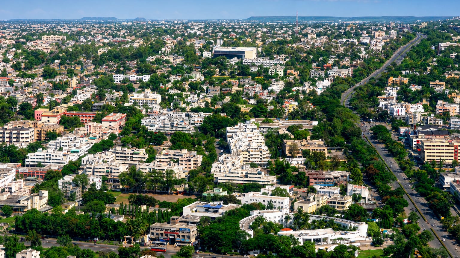Aerial view of the low-rise urban sprawl of Aurangabad, India, with cream buildings, greenery and distant hills