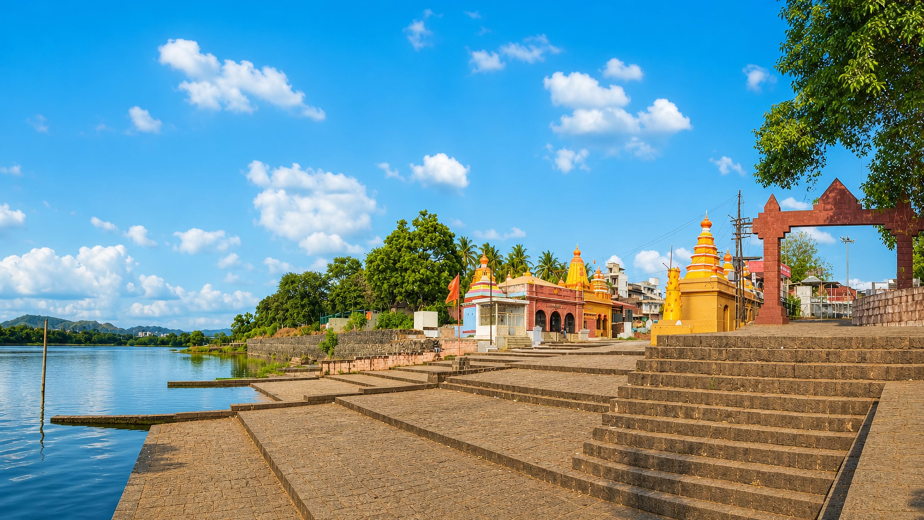 Stone ghat steps to the river at Karad, lined with yellow-spired temples and a red stone arch gateway