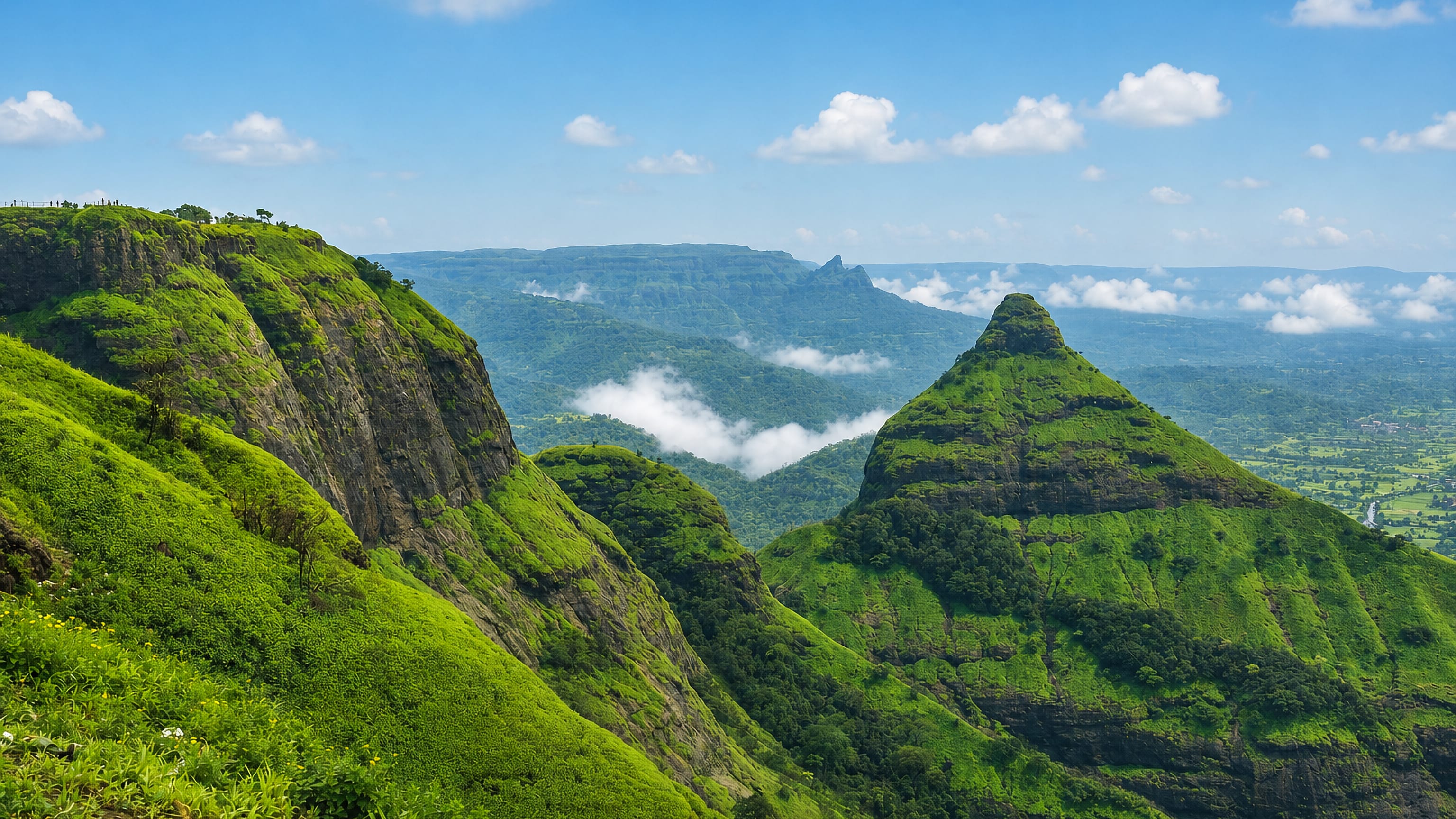 Green Western Ghats ridges and cloud-filled valleys above Lonavla, Maharashtra, under a bright monsoon sky.