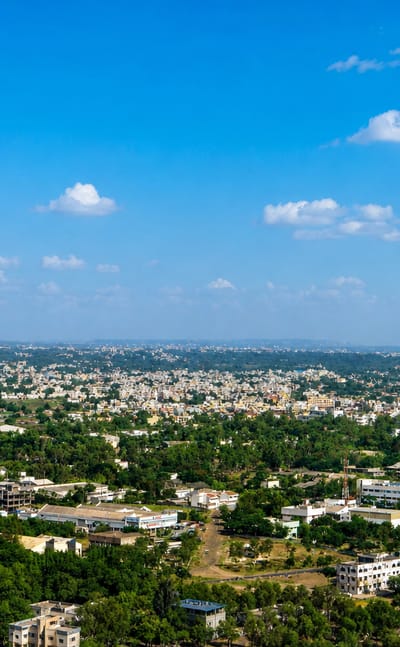 Aerial view of Nashik's tree-filled low-rise sprawl stretching to the horizon under a bright blue sky.