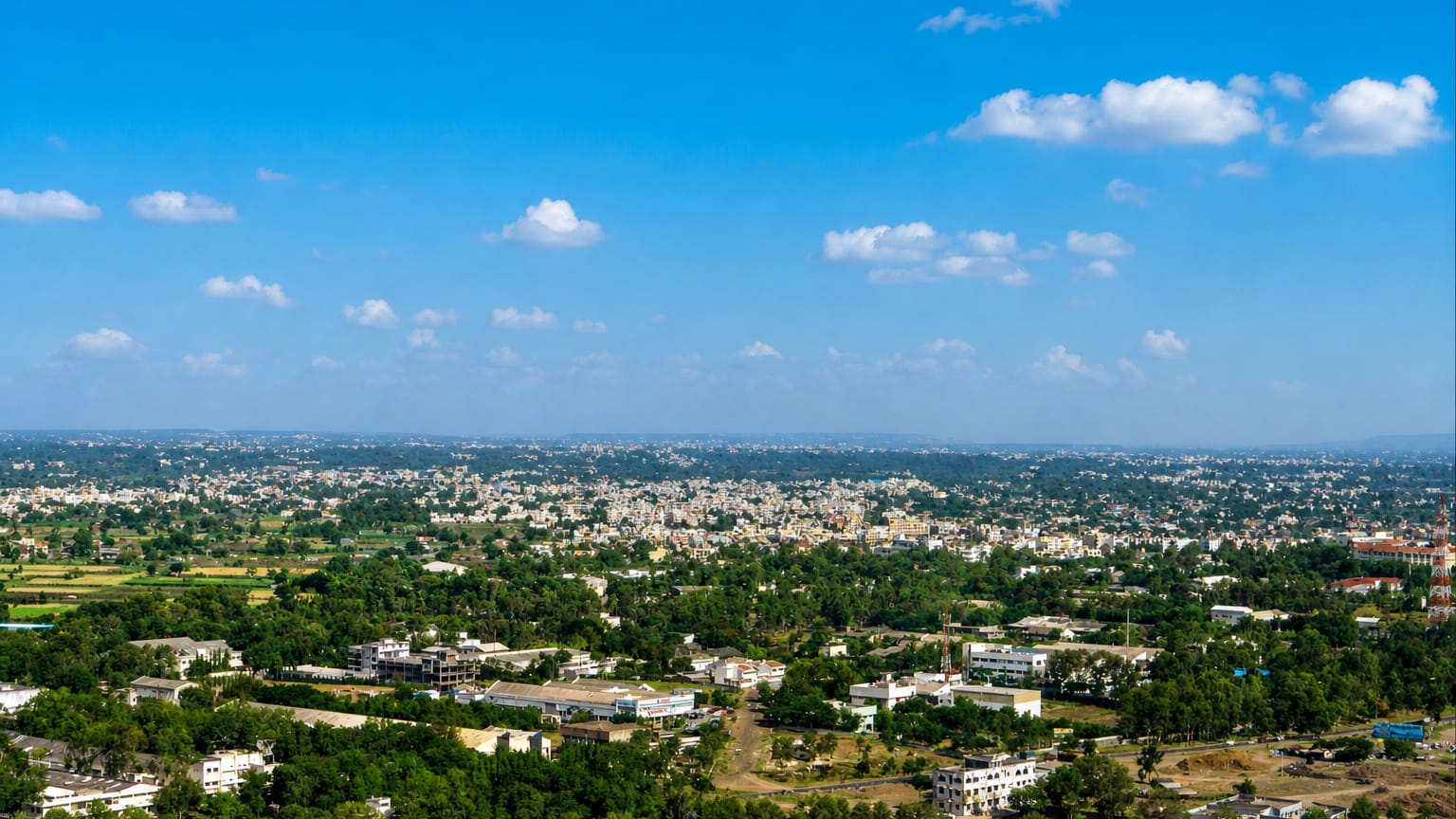 Aerial view of Nashik's tree-filled low-rise sprawl stretching to the horizon under a bright blue sky.