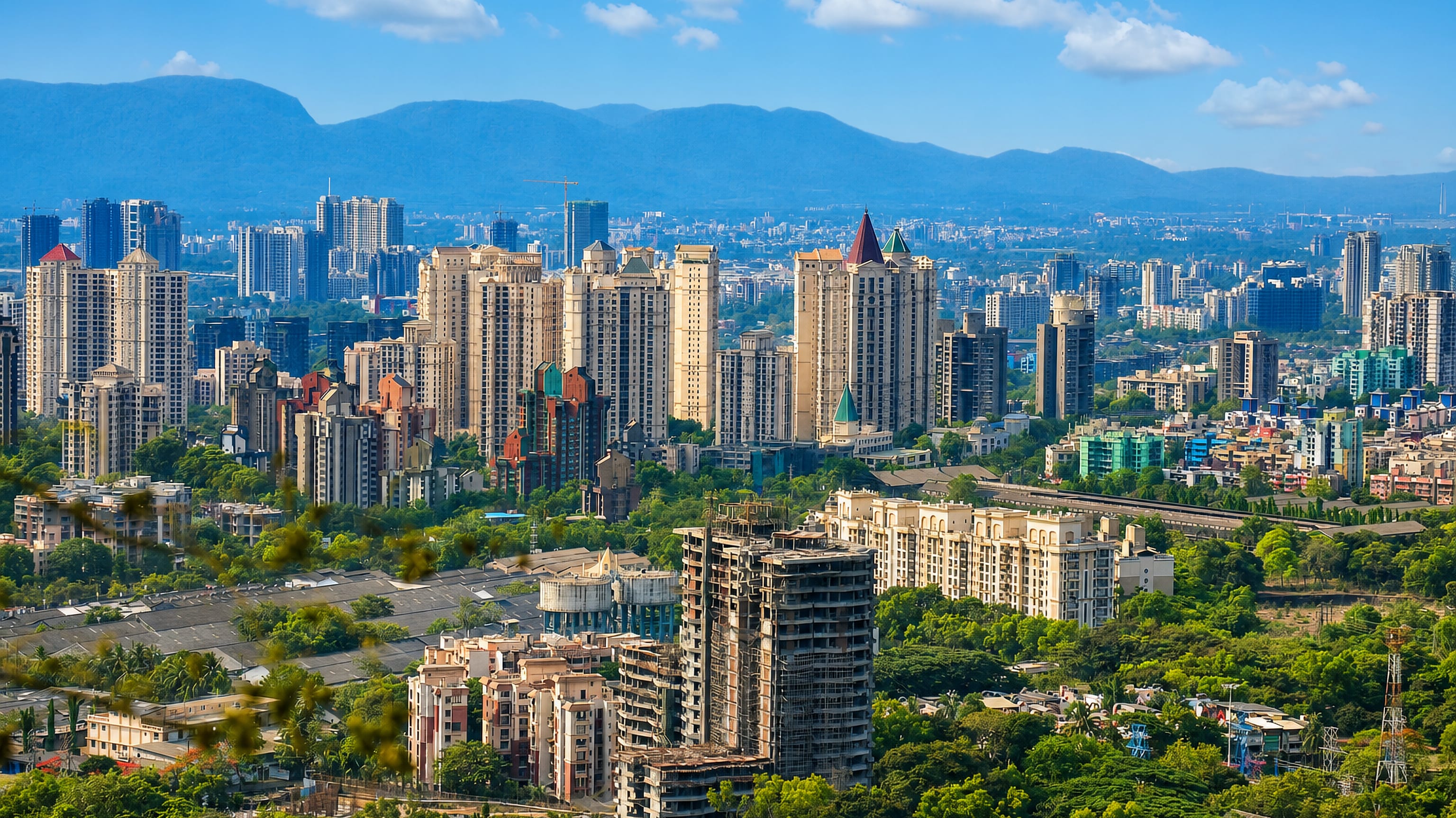 Thāne, India: clusters of high-rise apartment towers and dense greenery below hazy blue hills on a clear day.