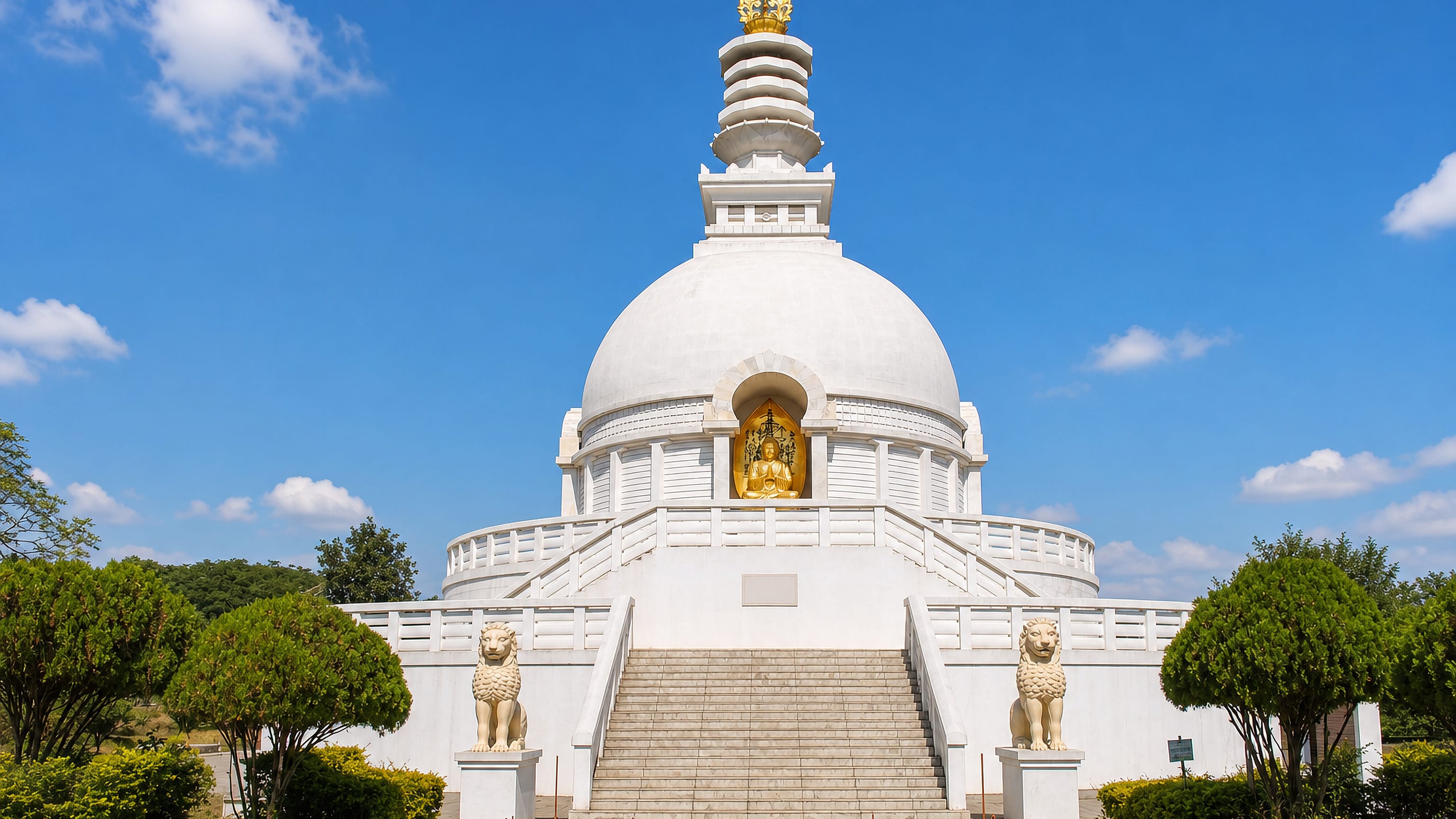 The white domed Vishwa Shanti Stupa peace pagoda with lion statues and a golden Buddha, Wardha, India.
