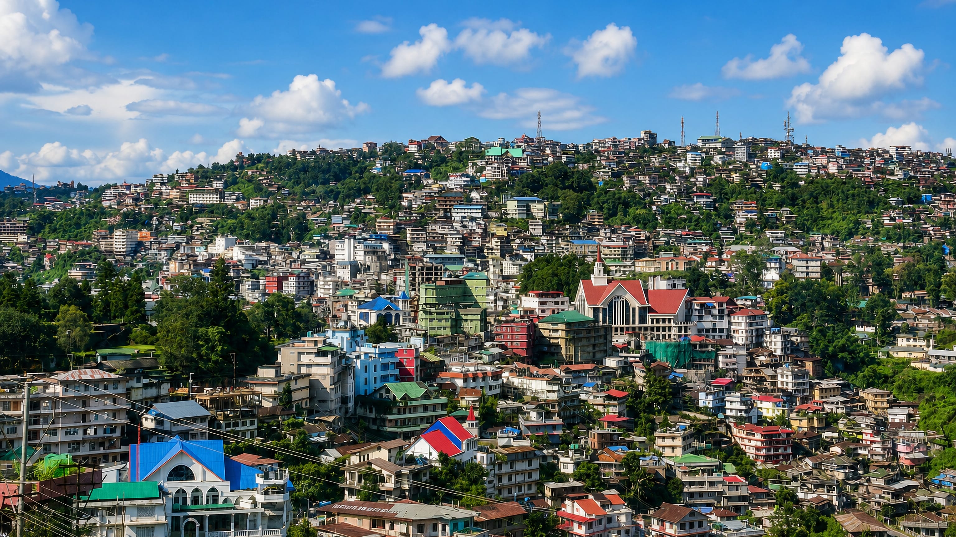 Hillside sprawl of Kohima, Nagaland, with brightly roofed houses climbing forested ridges around a large church.