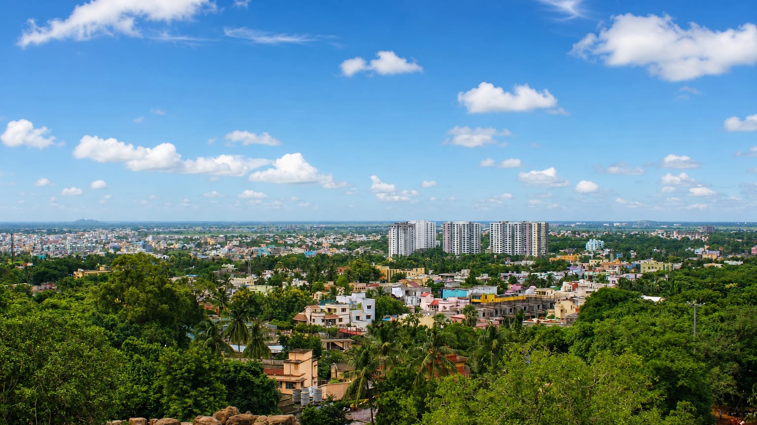 Green cityscape of Bhubaneswar with apartment towers and low houses seen from a rocky hill in Odisha.