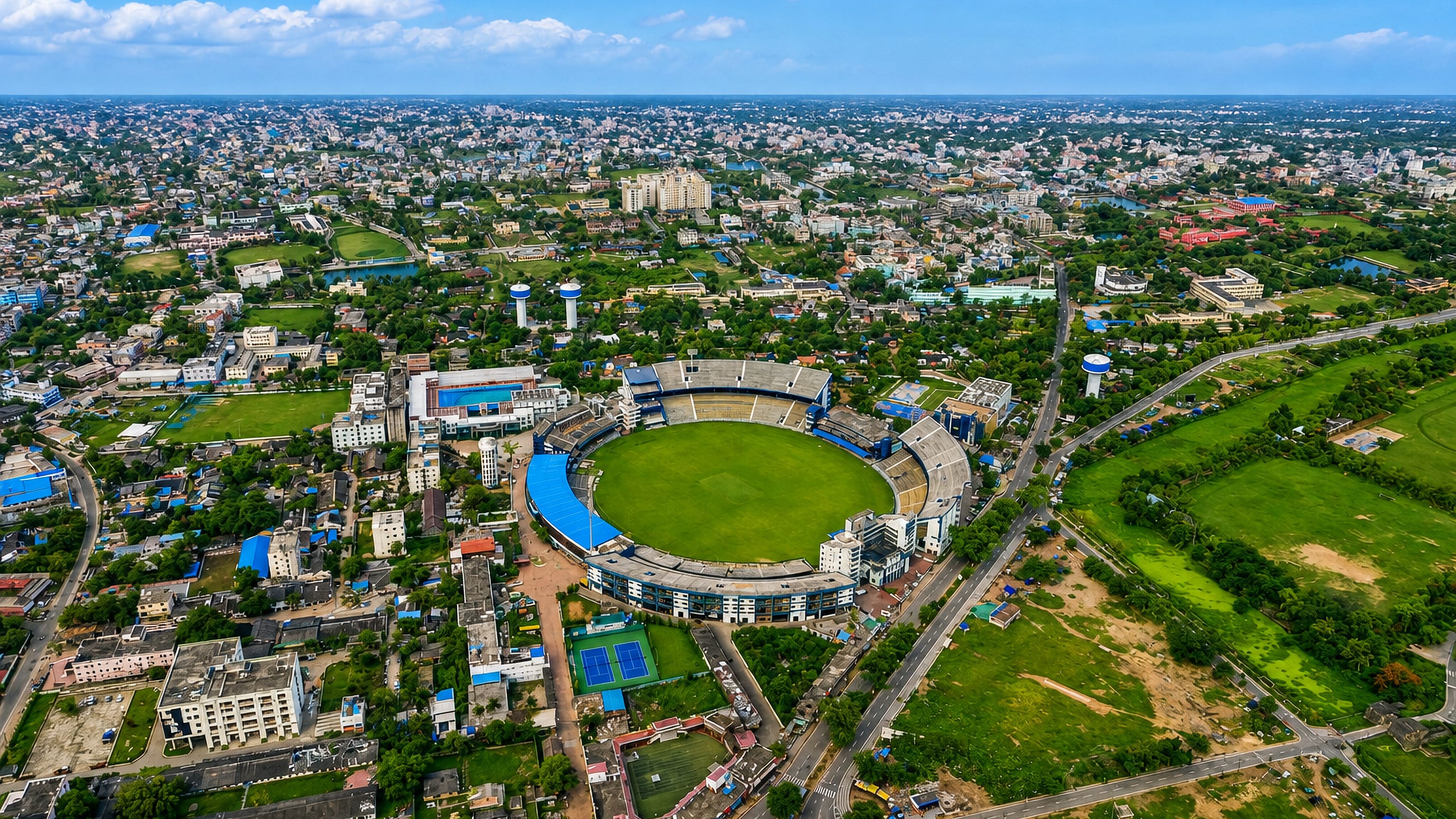 Aerial view of Cuttack, India, centred on its oval cricket stadium ringed by dense low-rise rooftops.