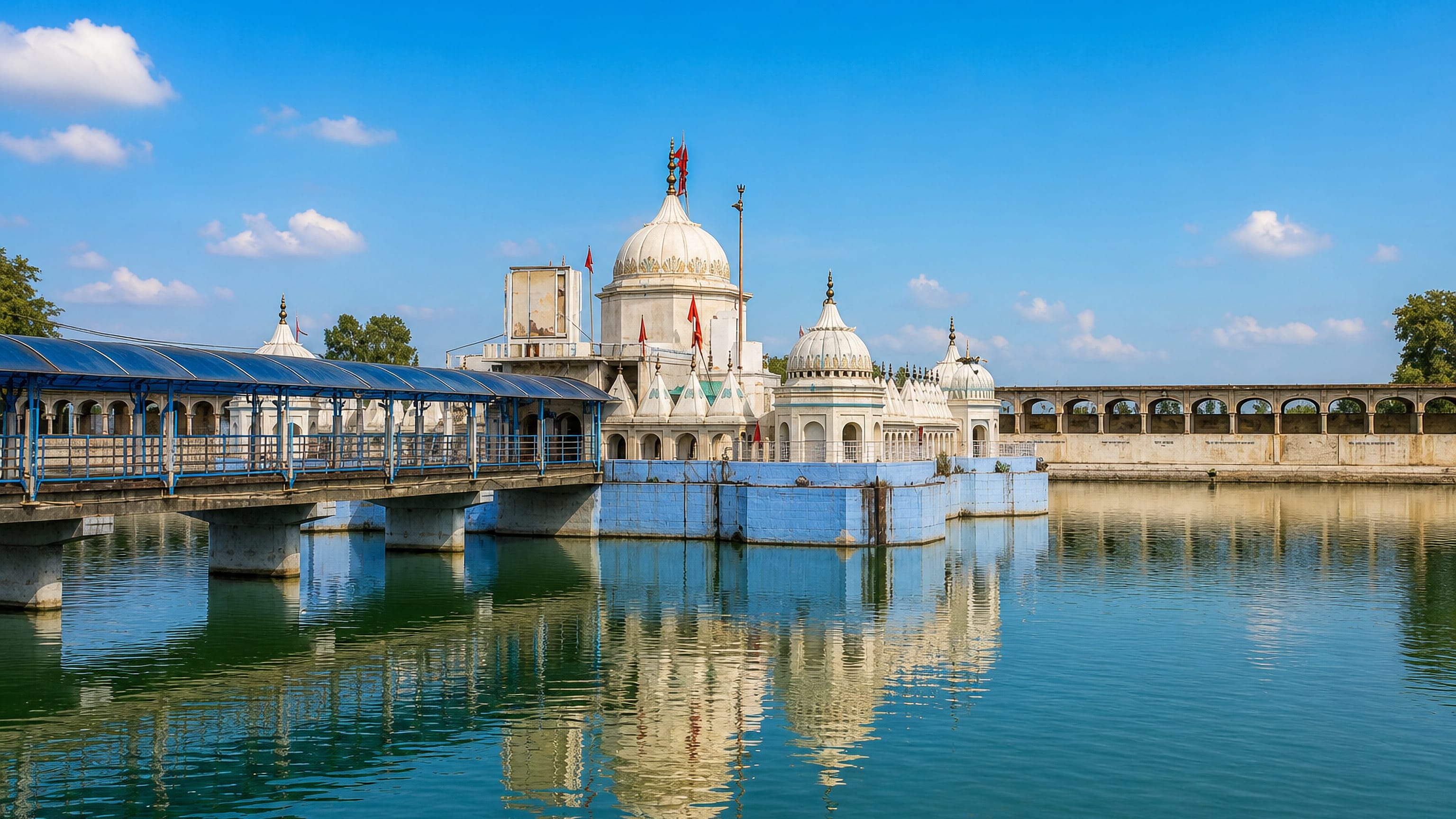 White-domed temple set in its walled water tank and reached by a covered walkway in Batala, Punjab.