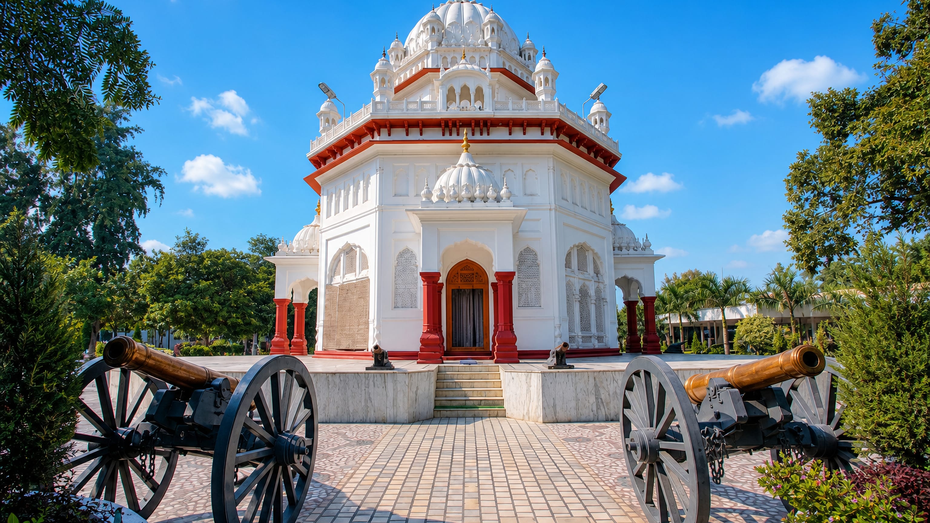 White-domed memorial flanked by two antique field cannons in a garden setting in Firozpur, Punjab.