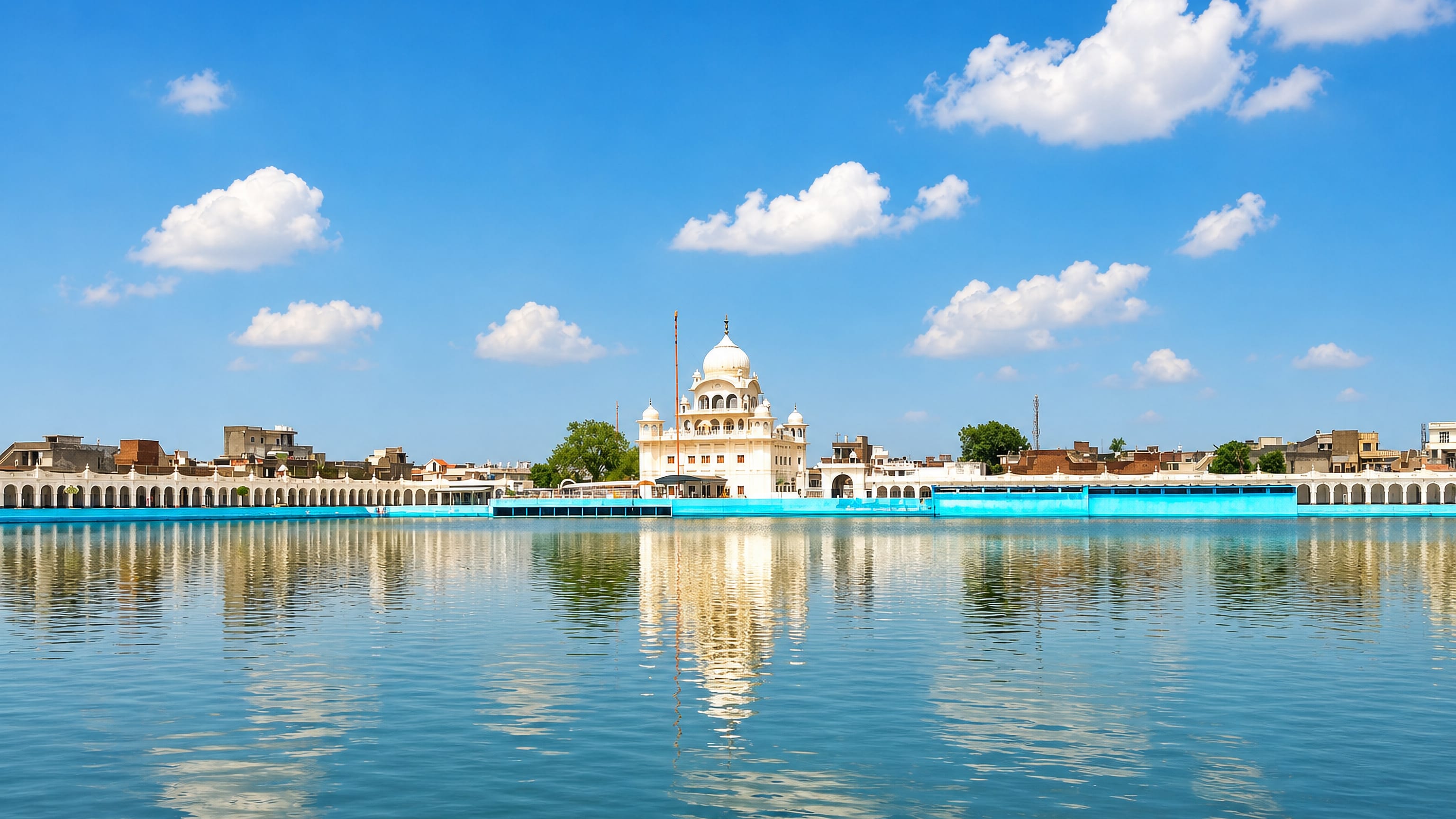 White-domed gurdwara mirrored in the great sarovar tank at Sri Muktsar Sahib, Punjab, under a clear sky.
