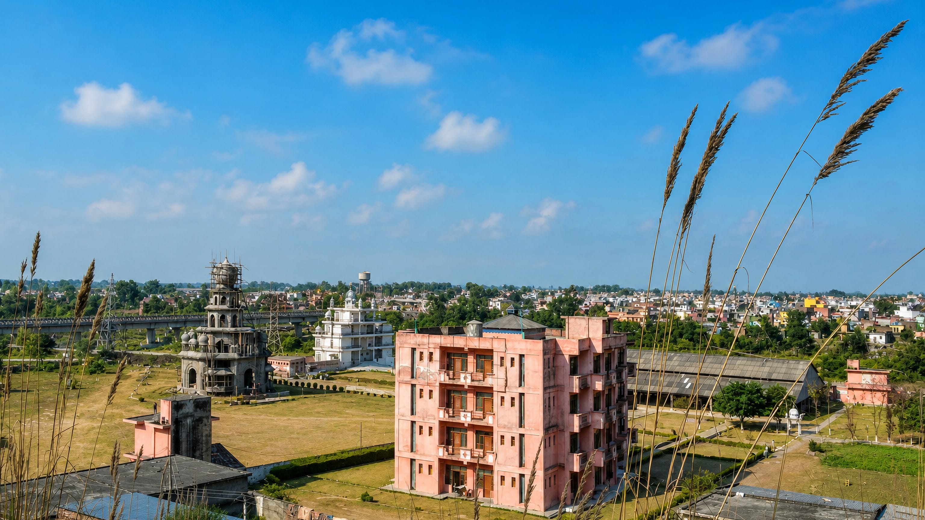 Rooftop view over Pathankot, Punjab, with a temple spire, a pink apartment block and a rail bridge beyond.