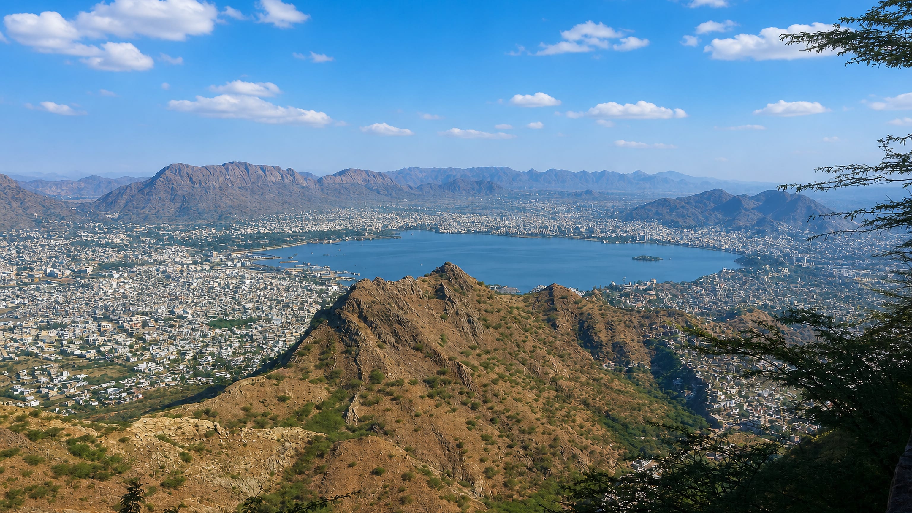Ana Sagar Lake ringed by Ajmer's dense white cityscape and the Aravalli hills, seen from a rocky ridge