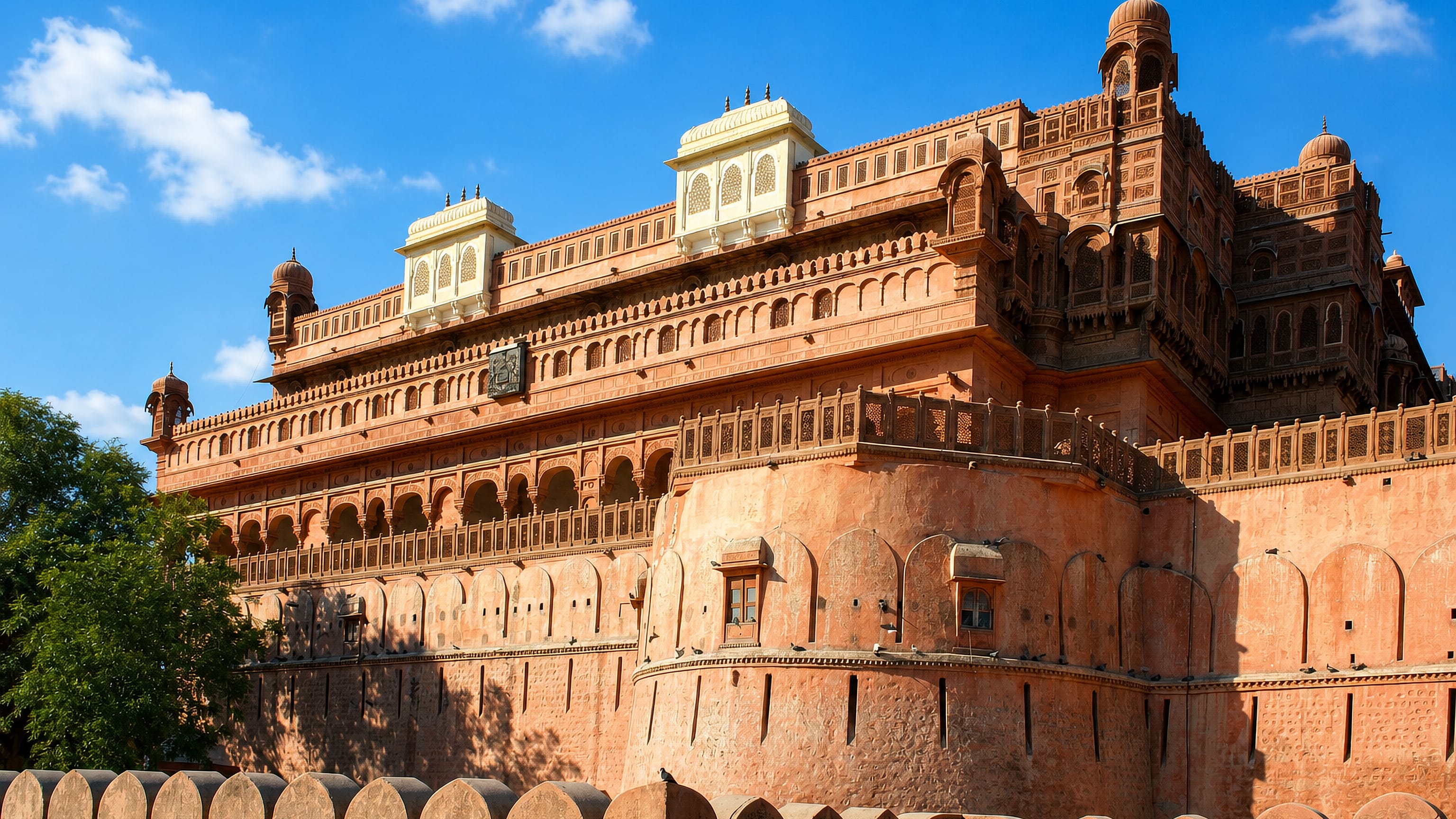 Ornate red sandstone ramparts and carved balconies of Junagarh Fort under blue sky in Bikaner, Rajasthan.